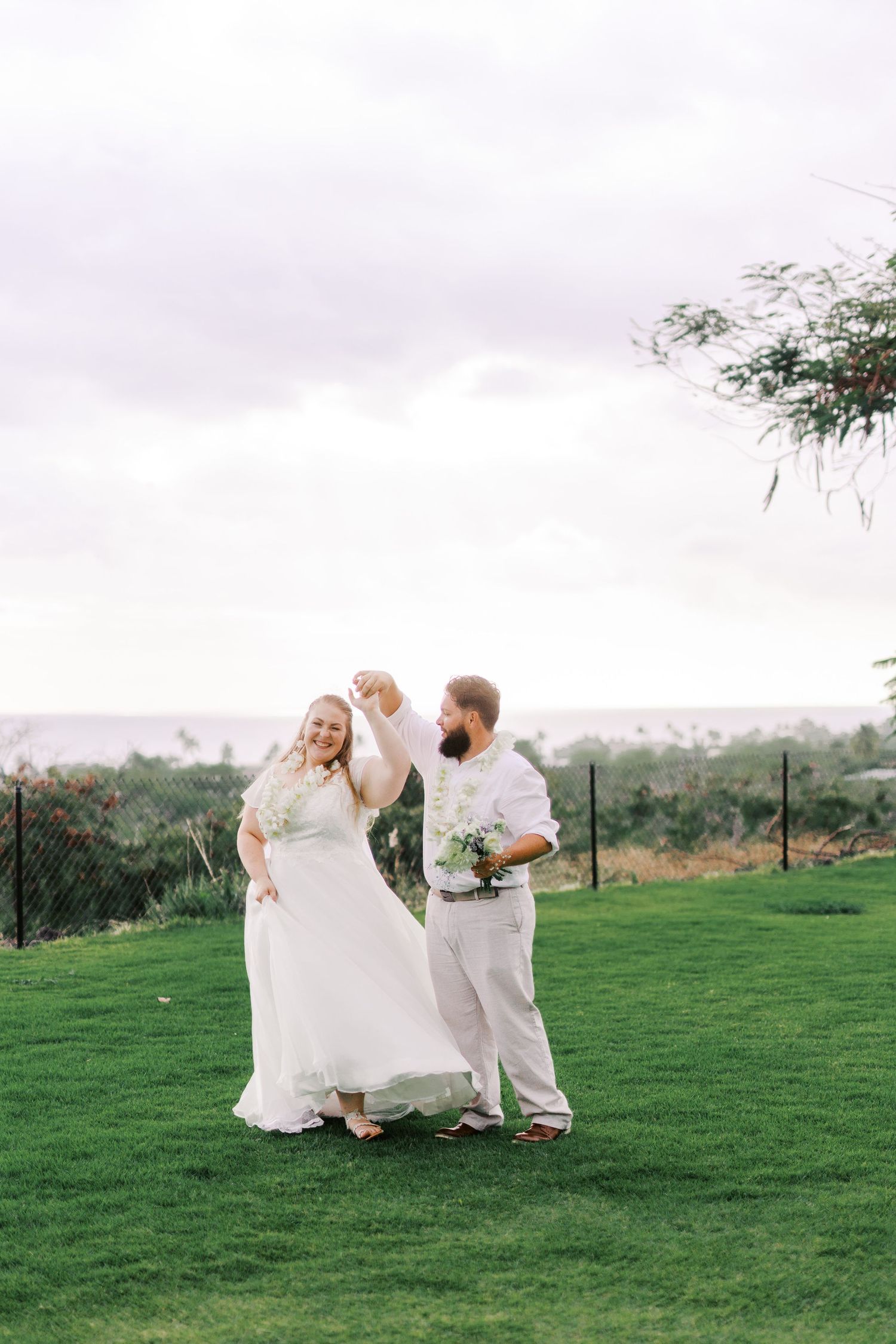Wedding couple dancing on grassy hilltop overlooking distant landscape.
