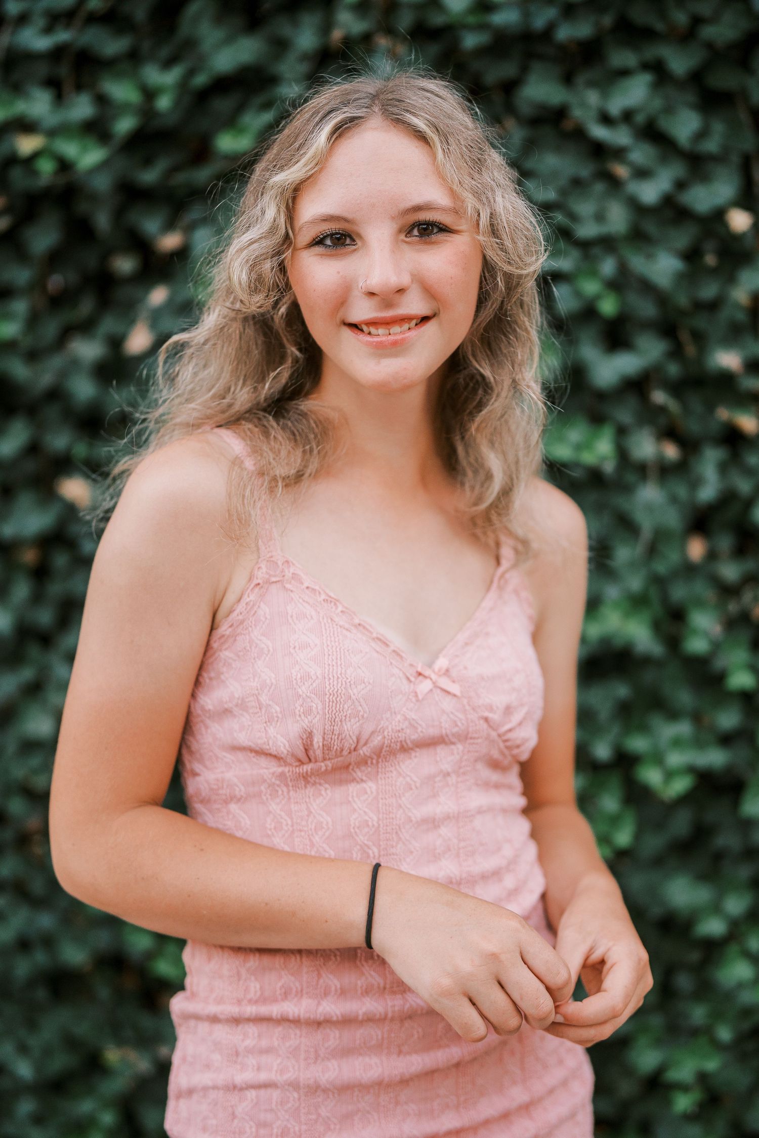 Woman in pink summer dress standing in front of lush green ivy wall.