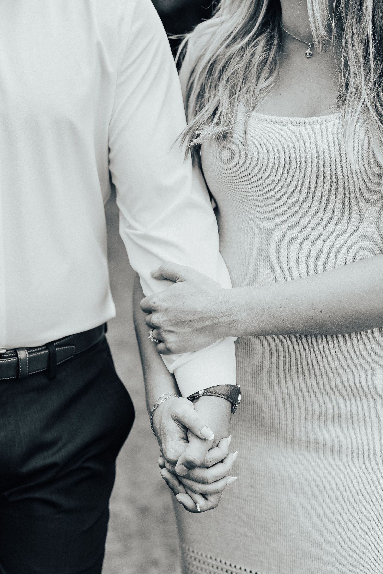 Close-up black and white photo of couple holding hands, with woman wearing ribbed dress and man in white shirt.