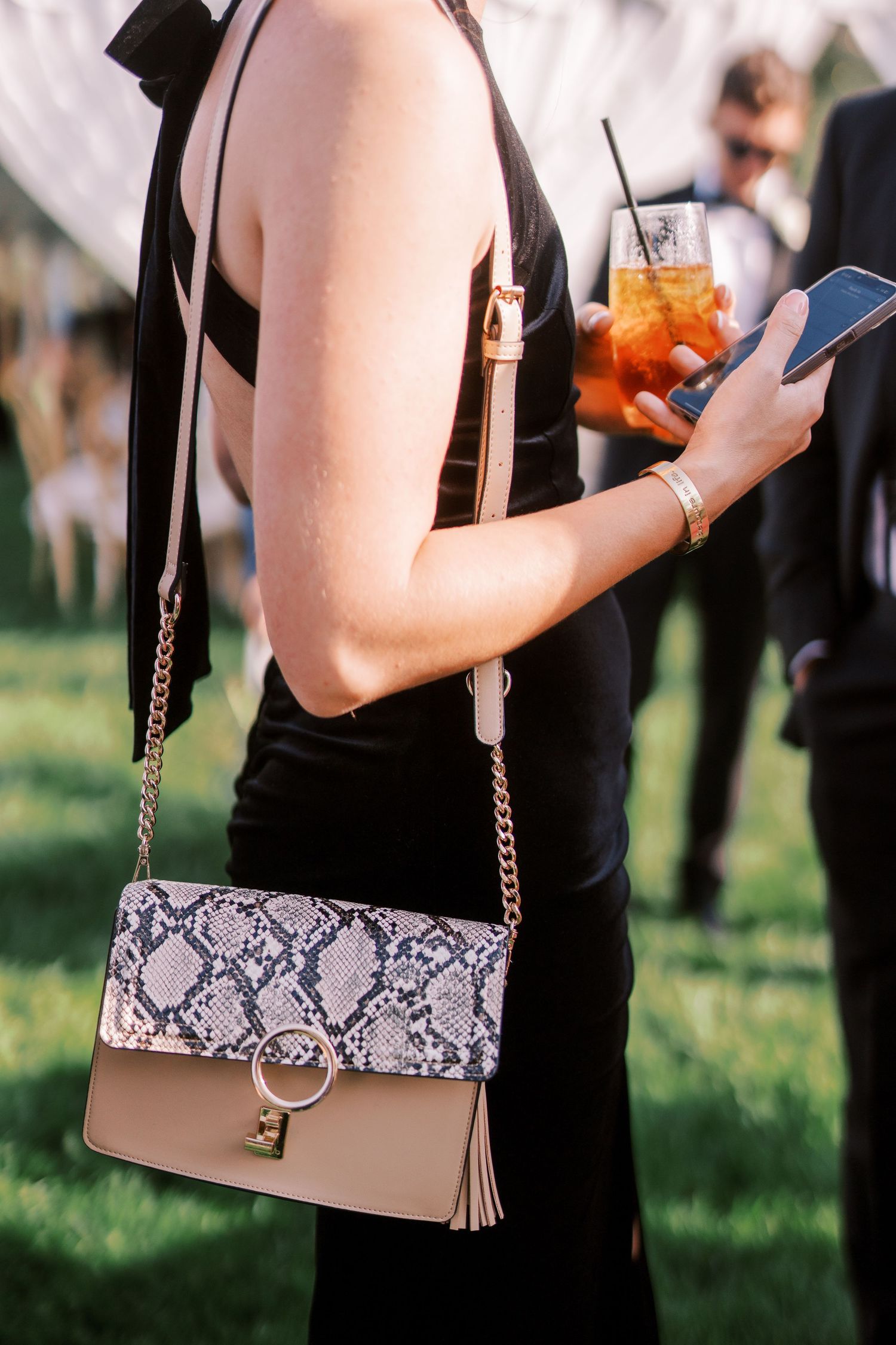 A stylish handbag with snakeskin print and brown leather details is displayed from multiple angles at an outdoor event.