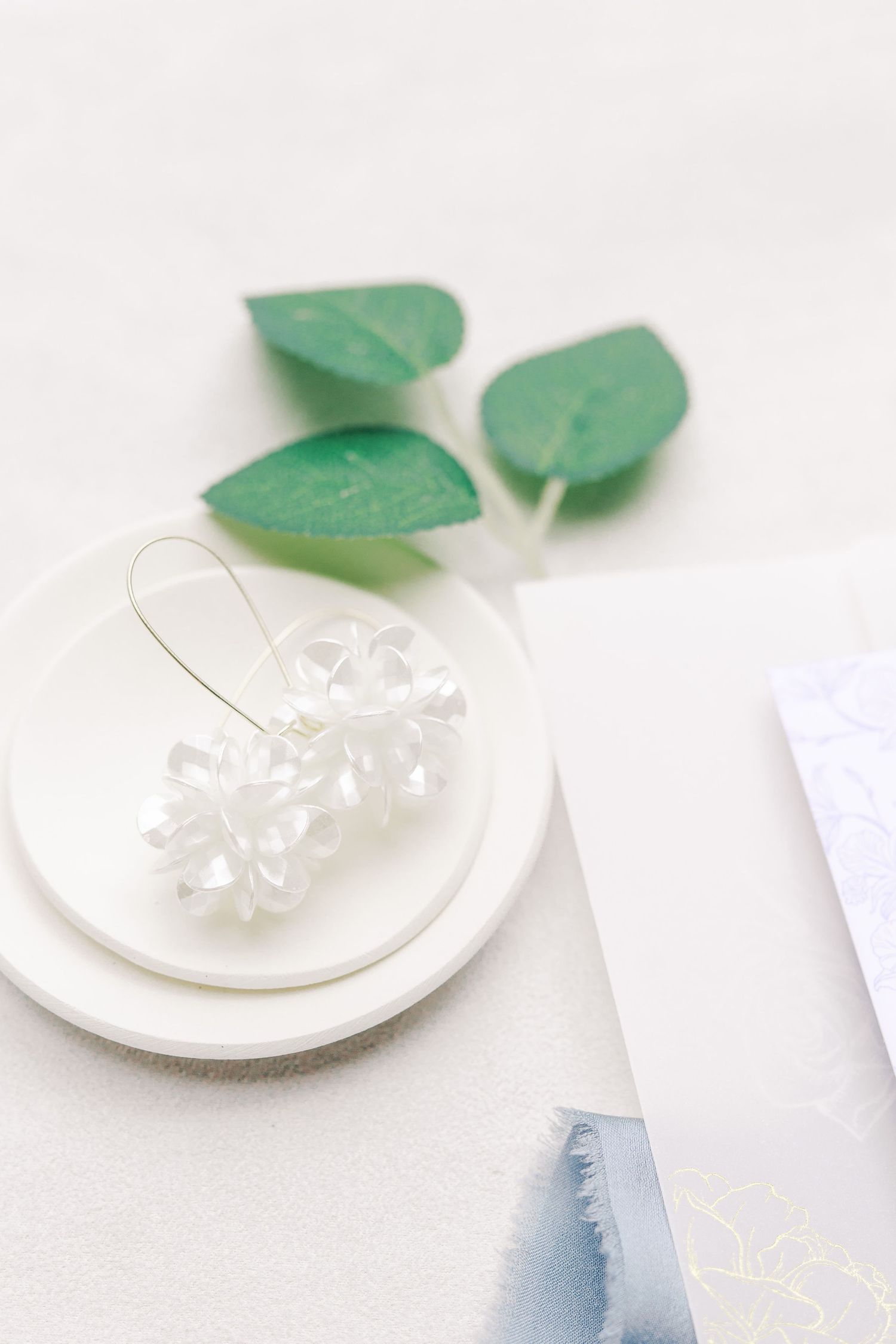 Minimalist wedding styling with white flower and green leaves on white plate.