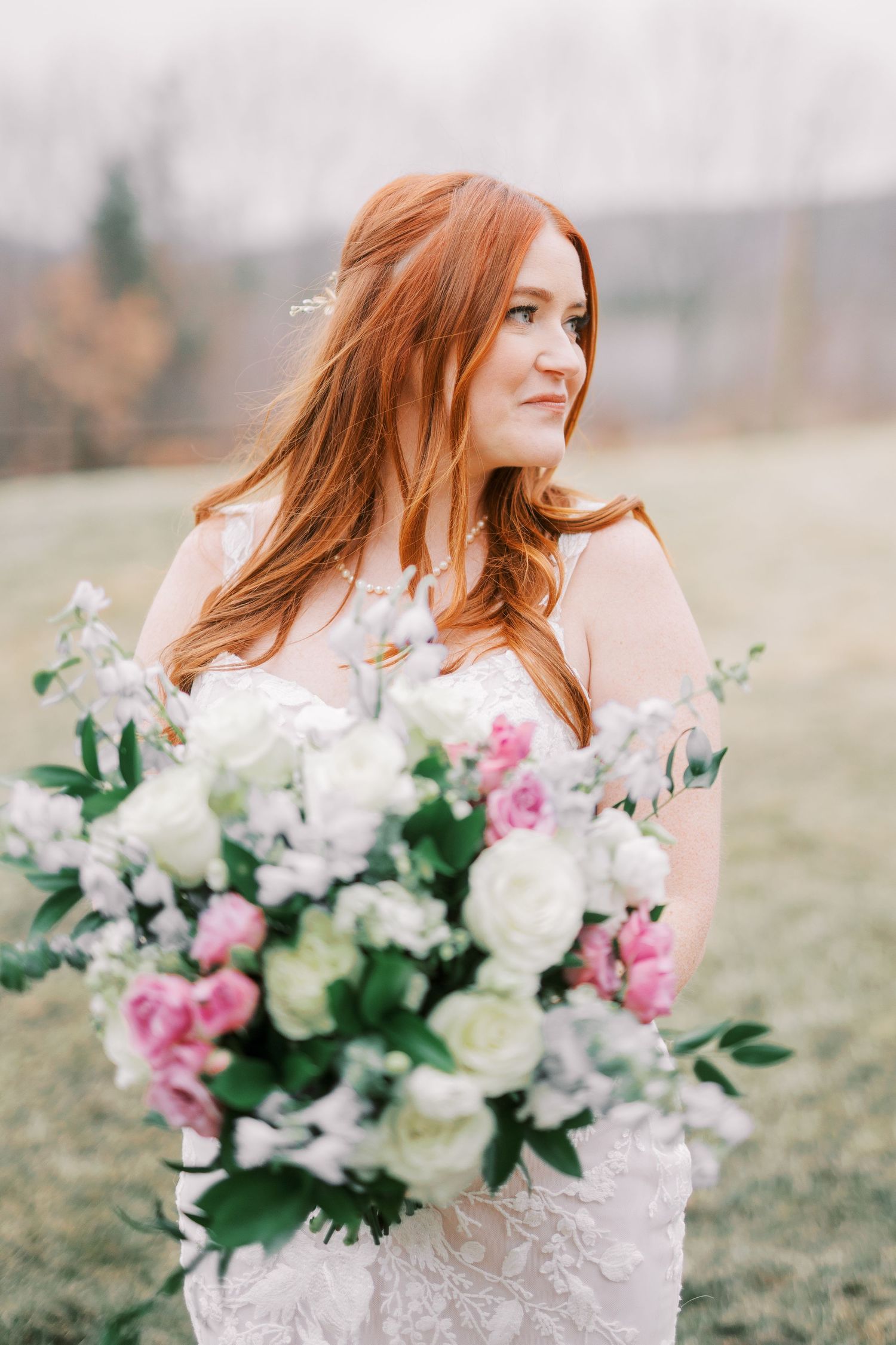 A bride in a white dress holds a romantic bouquet with pink and white flowers against a misty outdoor backdrop.