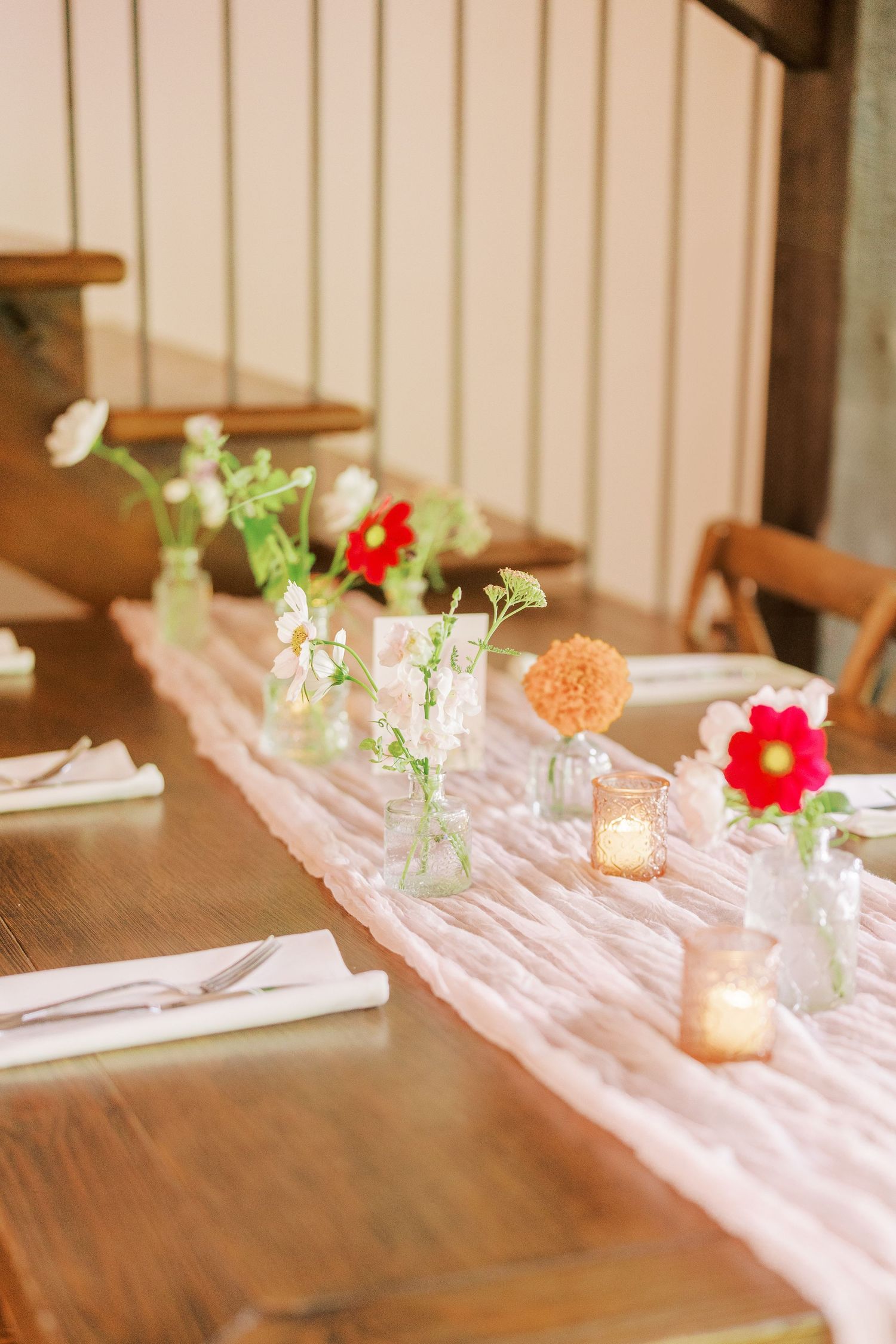 Romantic table setting with pink runner, small vases of flowers, and glowing candles.