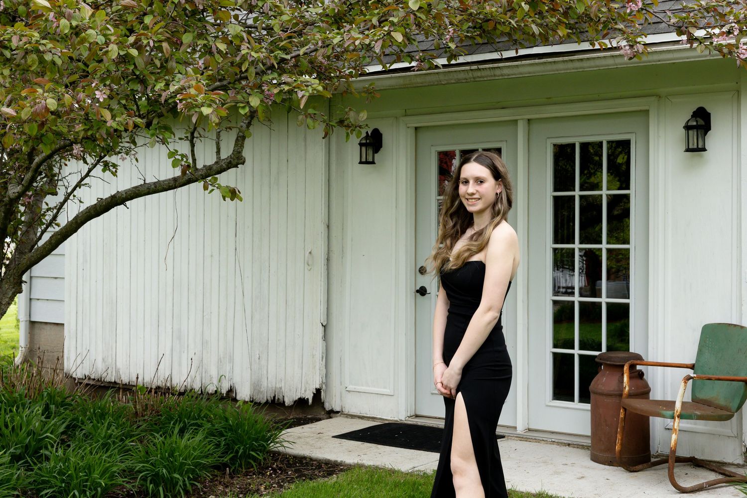 An elegant black evening gown stands in contrast with a white farmhouse exterior and French doors.