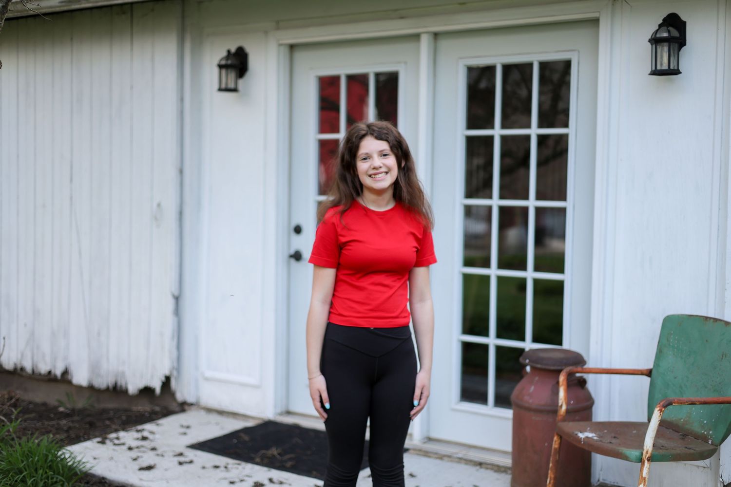 Person in red shirt and black pants standing in front of white door with black lanterns.