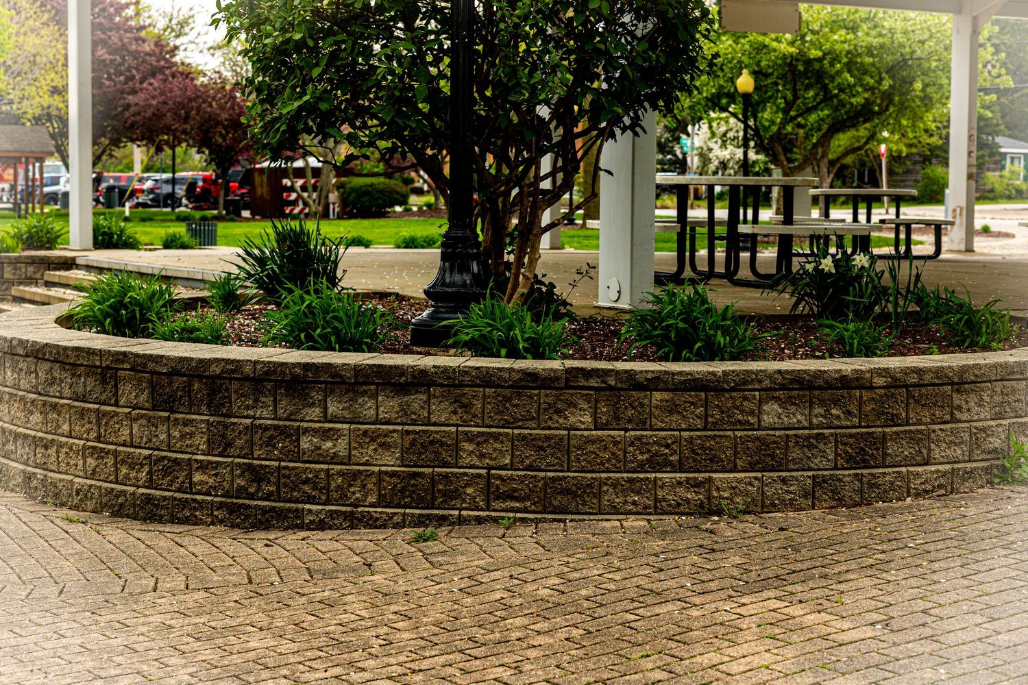 A curved stone retaining wall with decorative pattern surrounds a landscaped garden area with trees and plants.