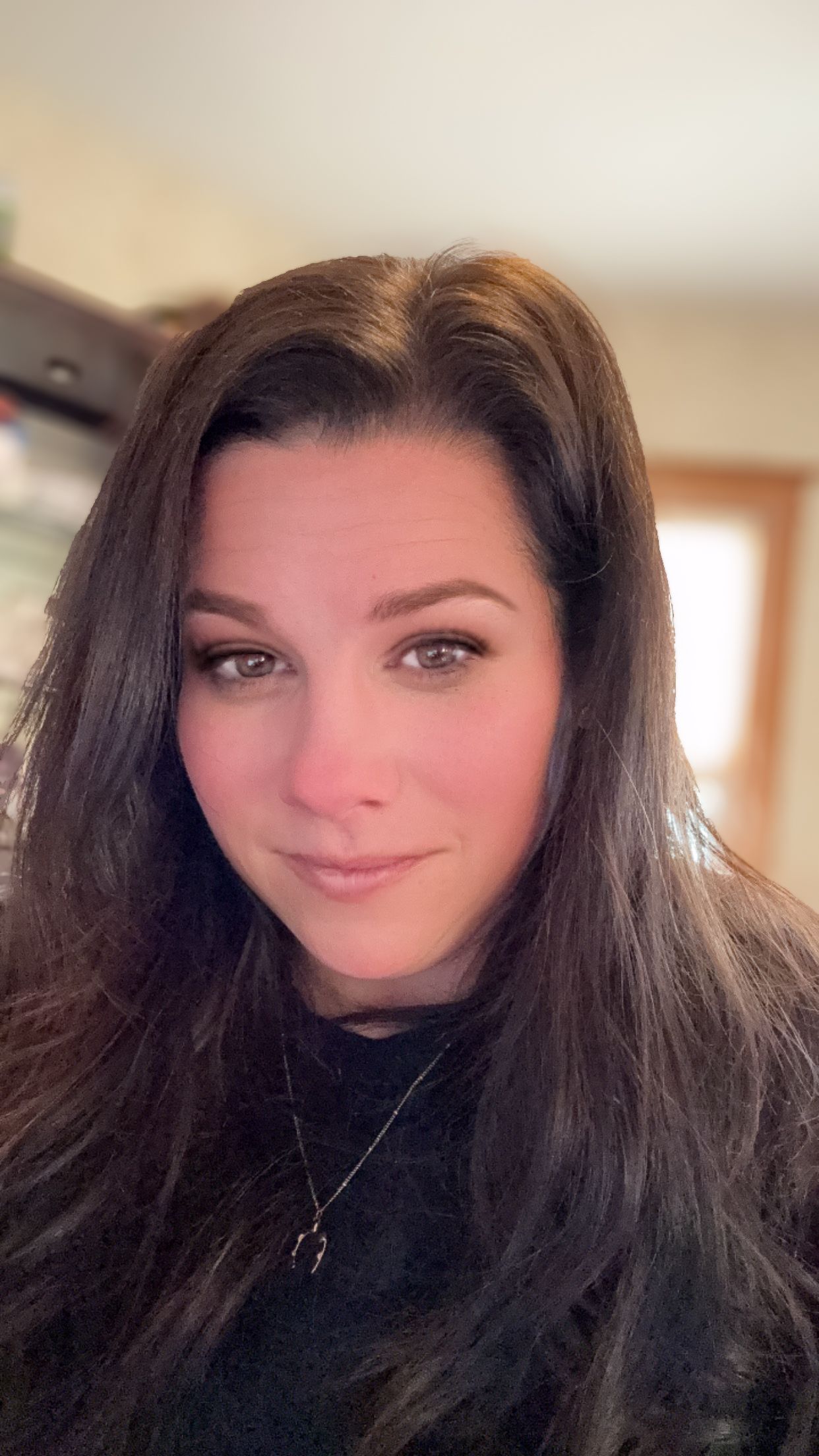 A woman with long dark hair and natural makeup wearing a black sweater smiles warmly at the camera.