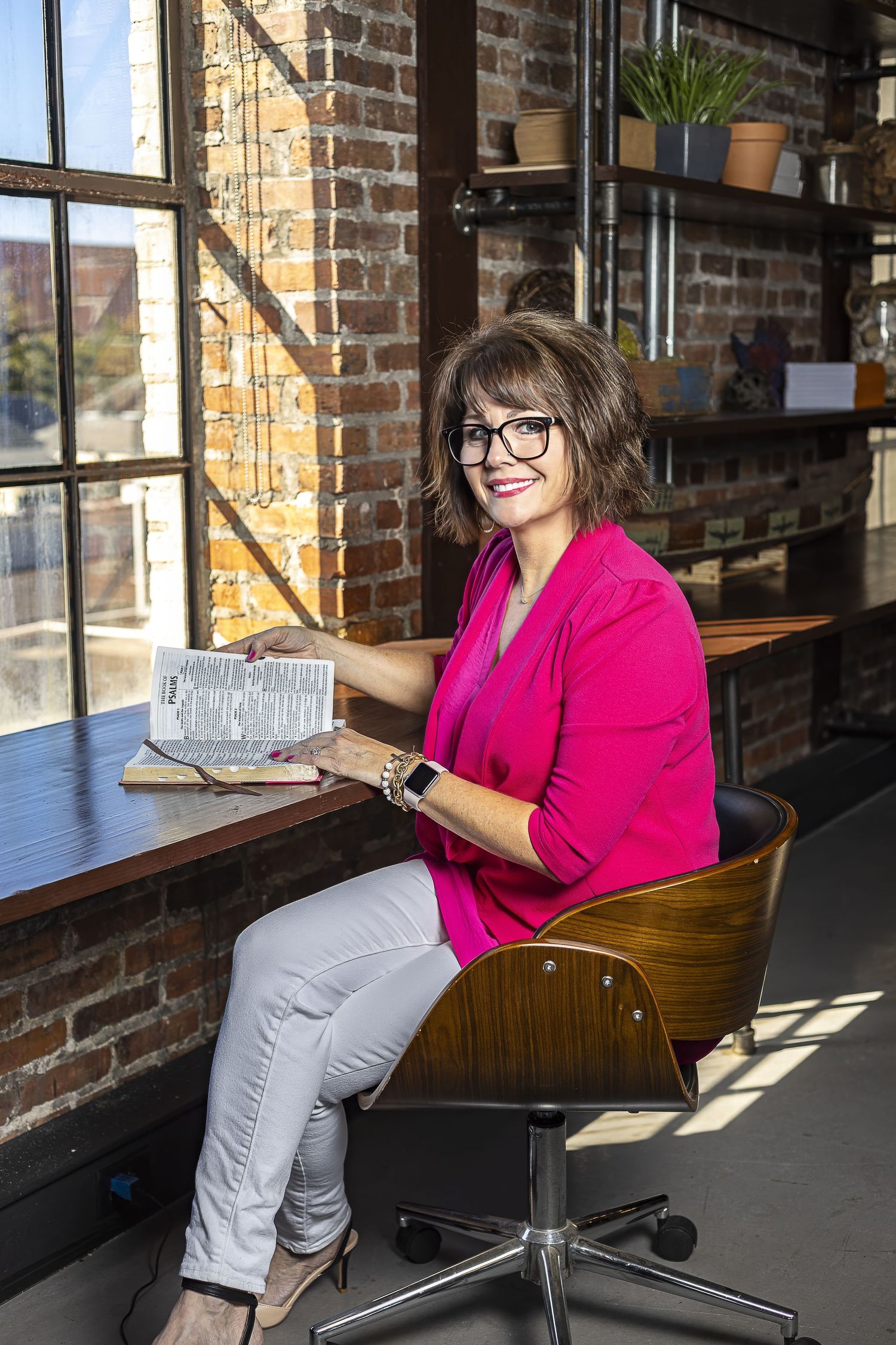 Professional working at desk in modern industrial office with exposed brick walls and natural lighting.