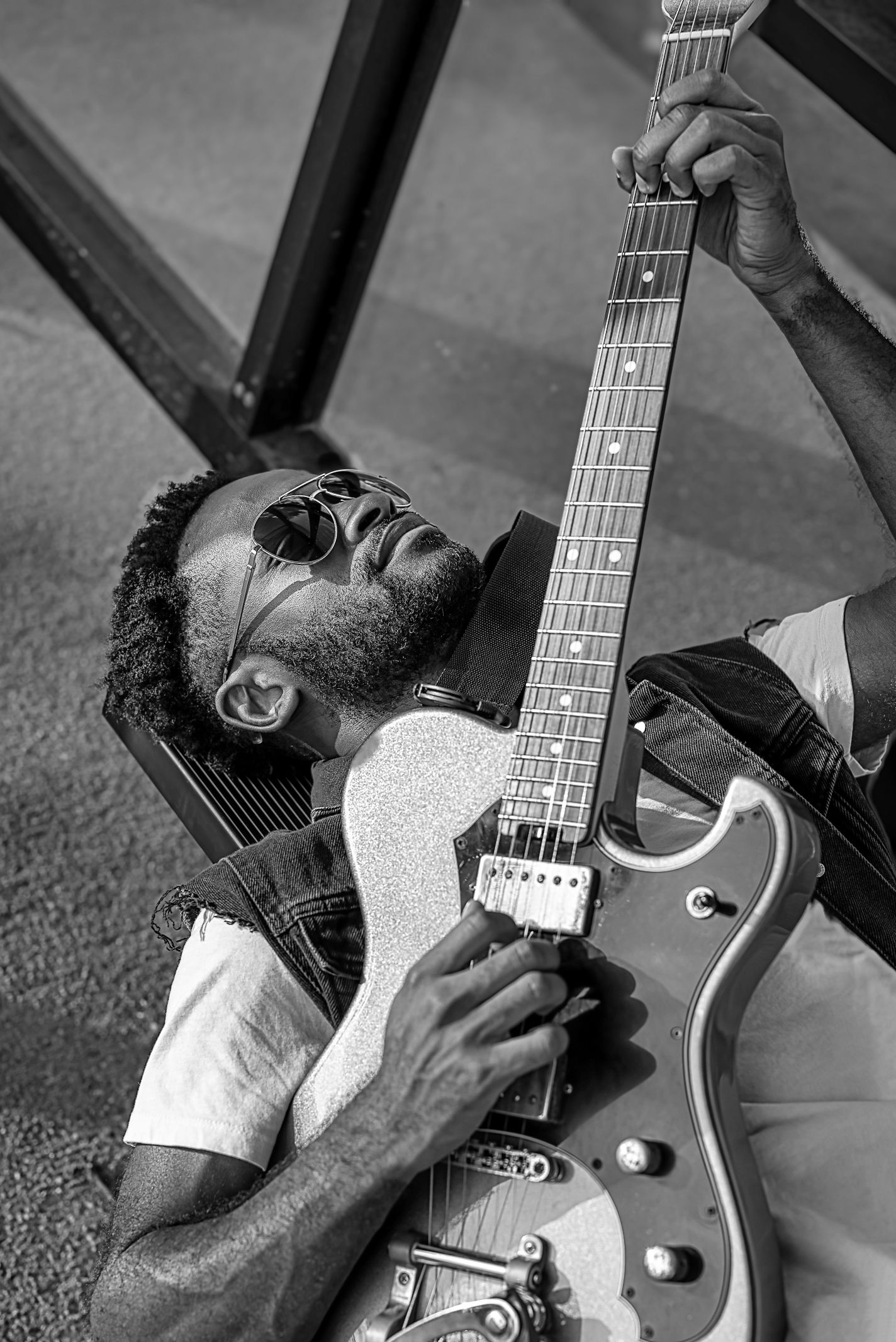 Musician plays electric guitar while lying down in dramatic black and white composition.