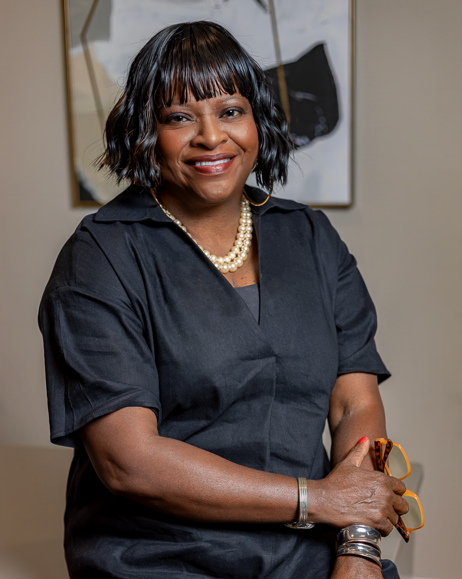 Professional portrait of person in black dress wearing pearl necklace and silver bracelet.