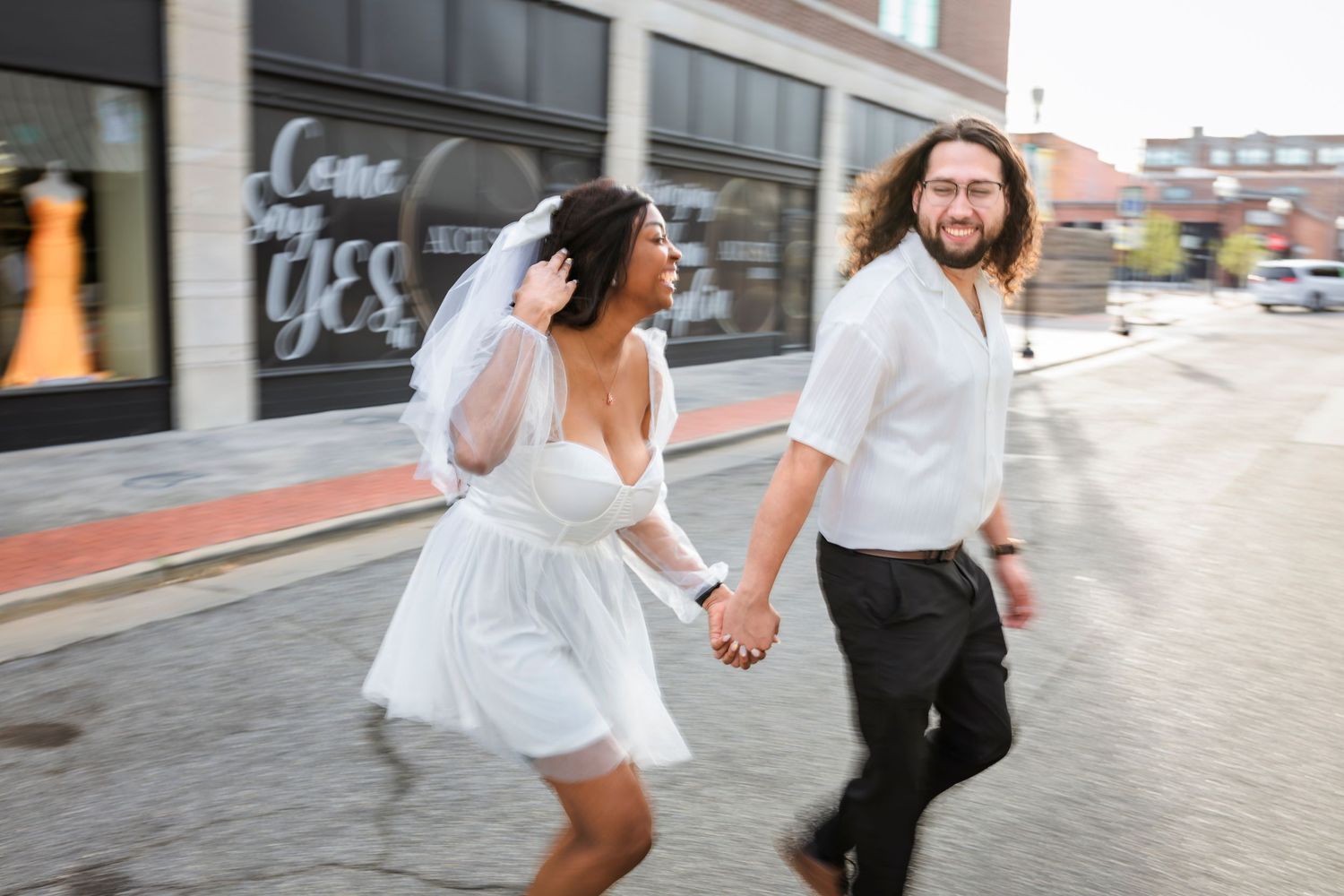 Joyful couple running together on downtown Joplin Missouri sidewalk, one wearing a white dress.