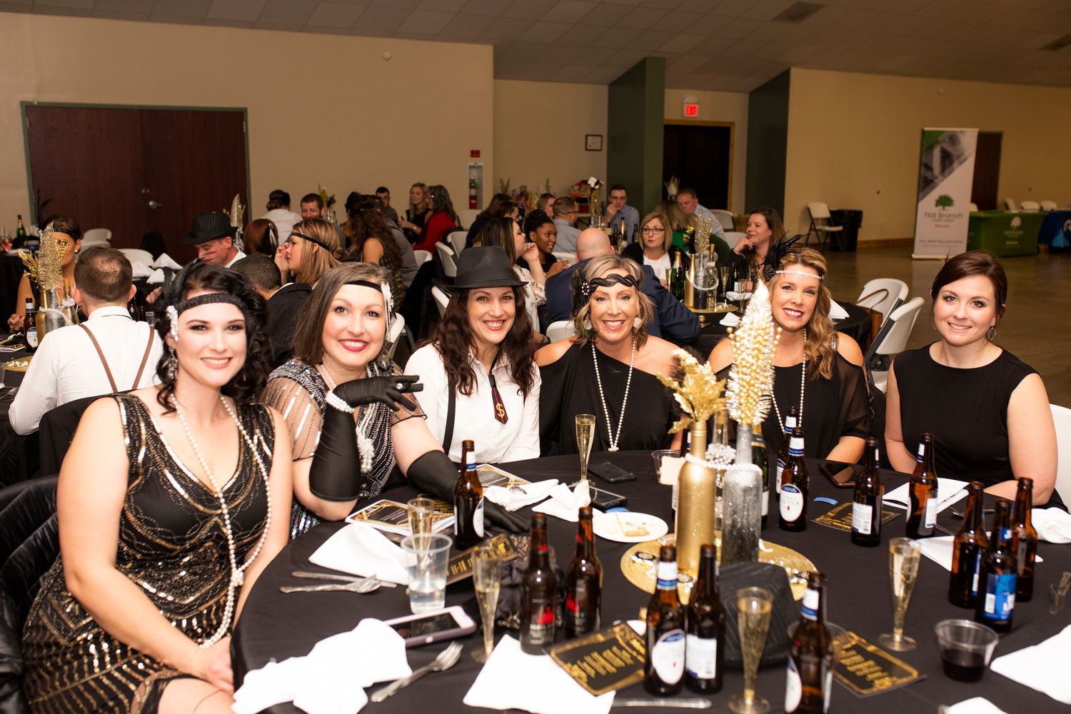 Group at a formal dinner event seated at tables with wine bottles and place settings in a banquet hall.
