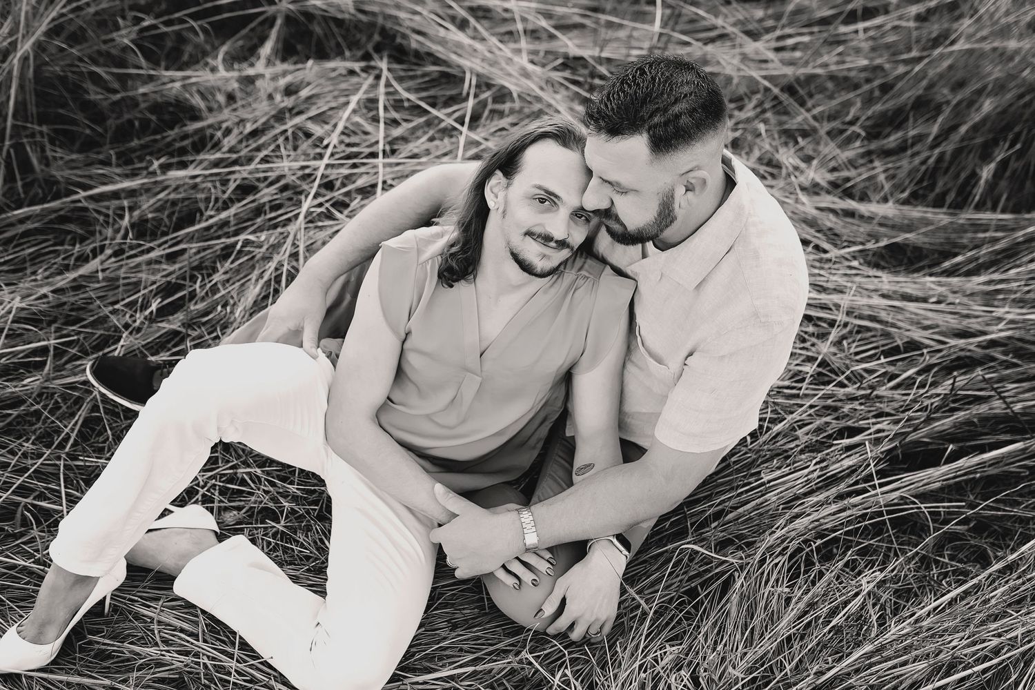 Gay couple in cozy pose sitting together in a field in Springfield Missouri during engagement shoot.