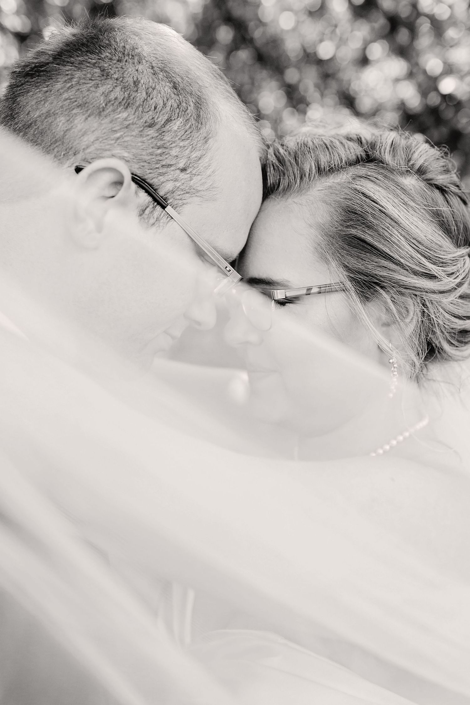 Black and white close-up photo of a couple sharing an intimate moment beneath a delicate veil at Timberline Barn in Buffalo Missouri.