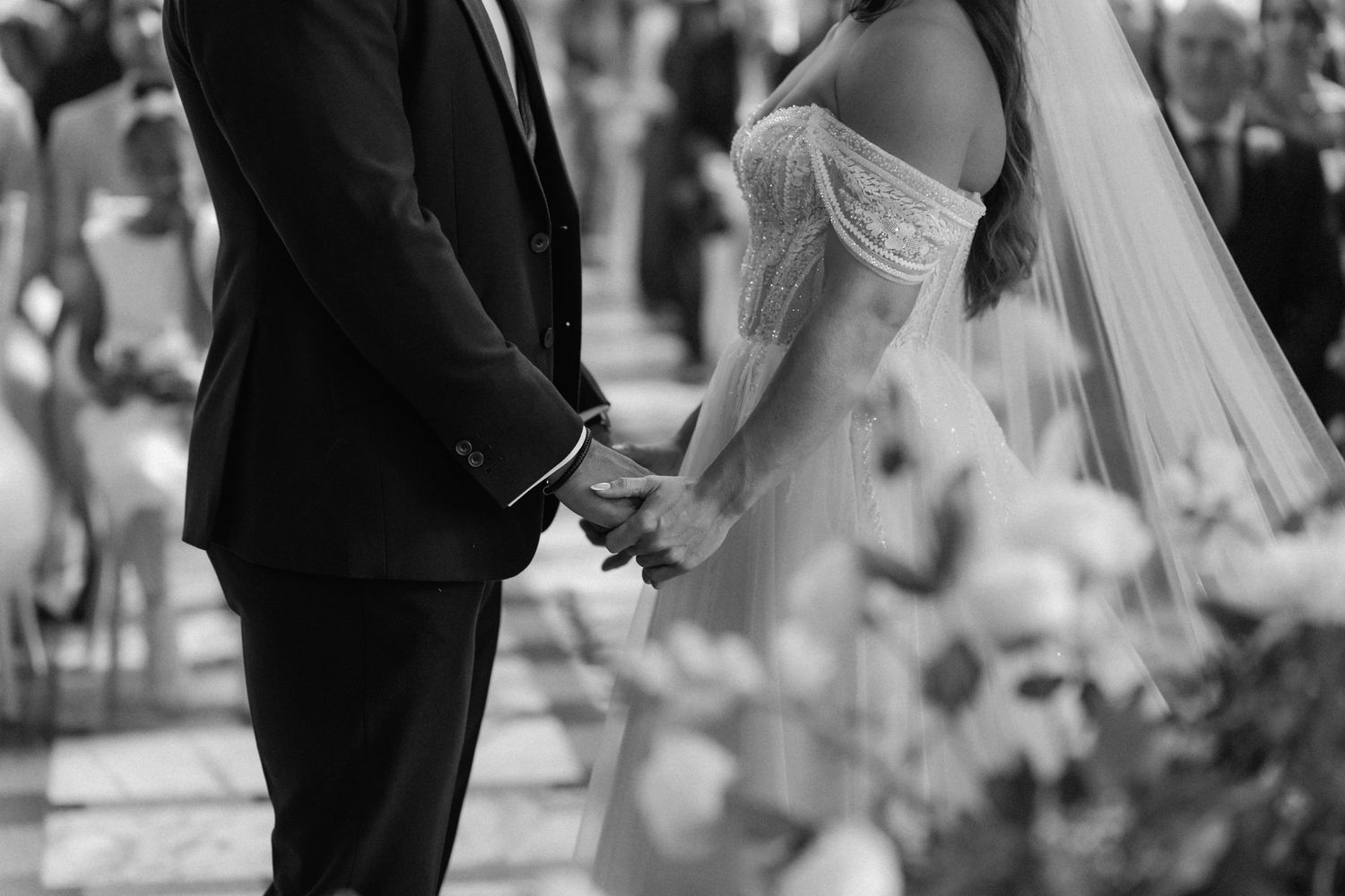 Close-up black and white shot of newlyweds holding hands during their ceremony.