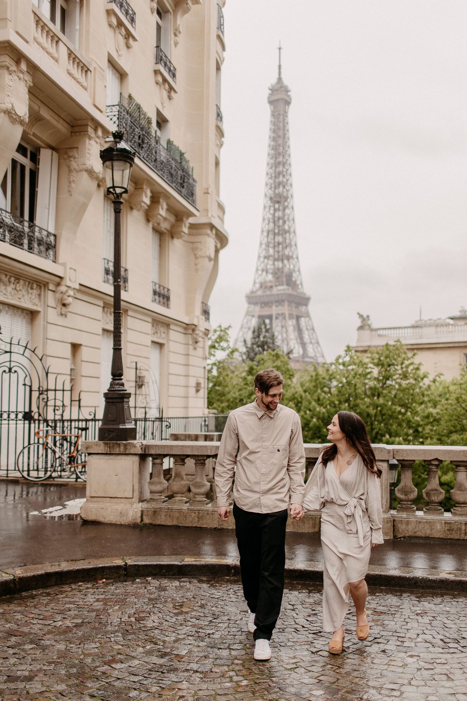 A couple strolling along a wet Parisian street with the Eiffel Tower visible in the background.