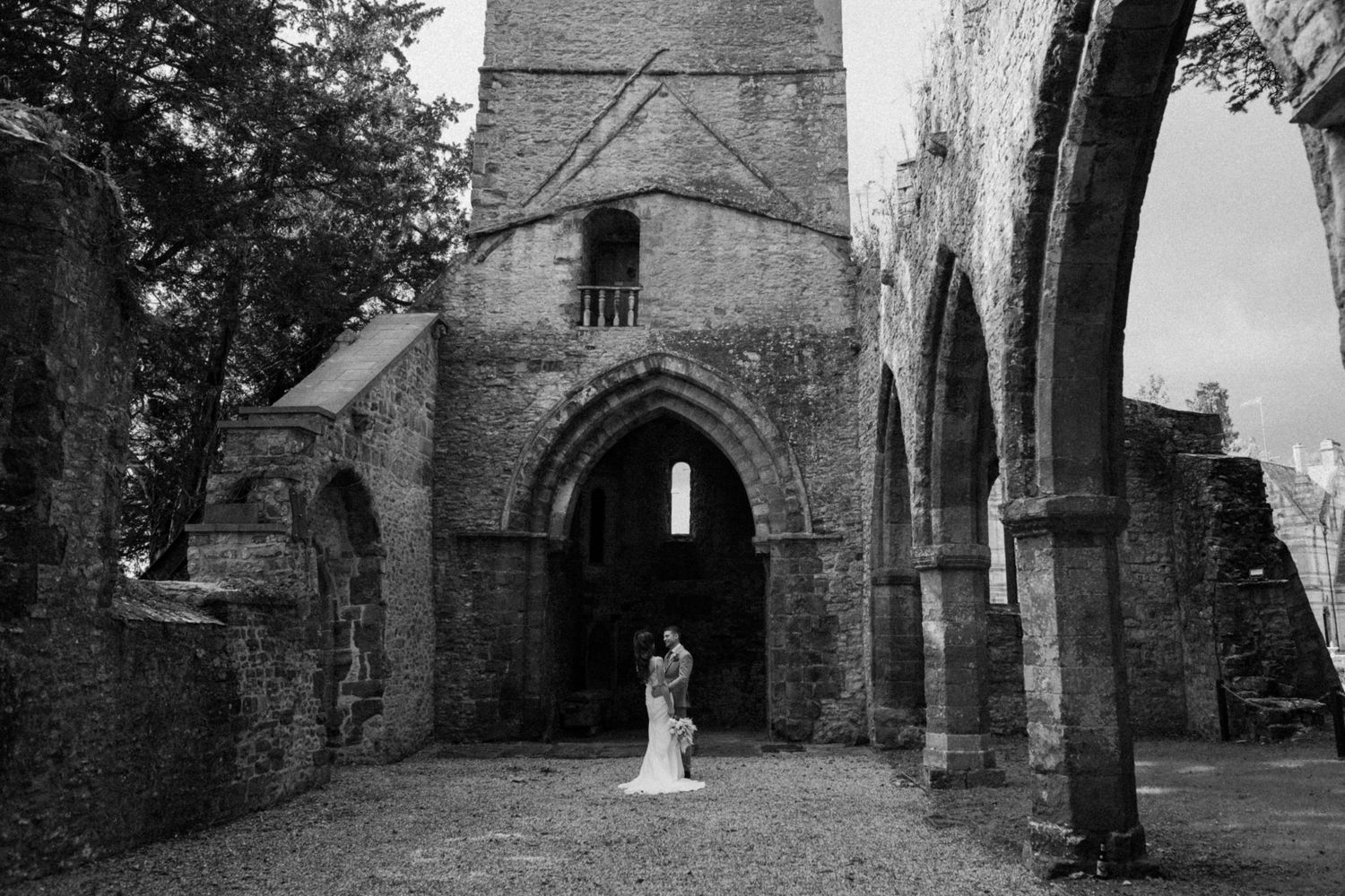 A black and white wedding photo taken through an ancient stone church archway at Ettington Park Hotel.