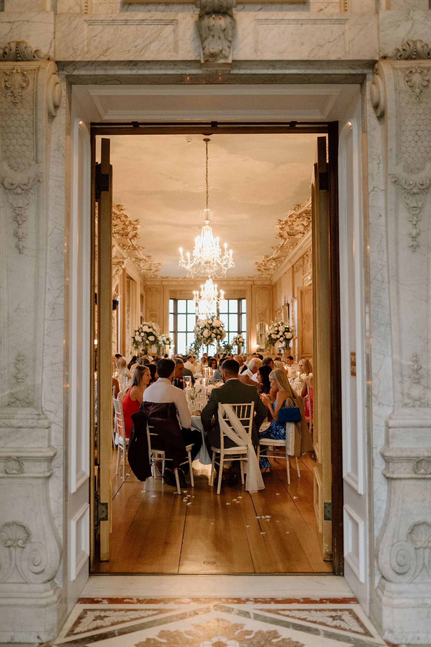 Elegant wedding reception dining room with crystal chandeliers and ornate white molding framing the entrance at Harlaxton Manor.