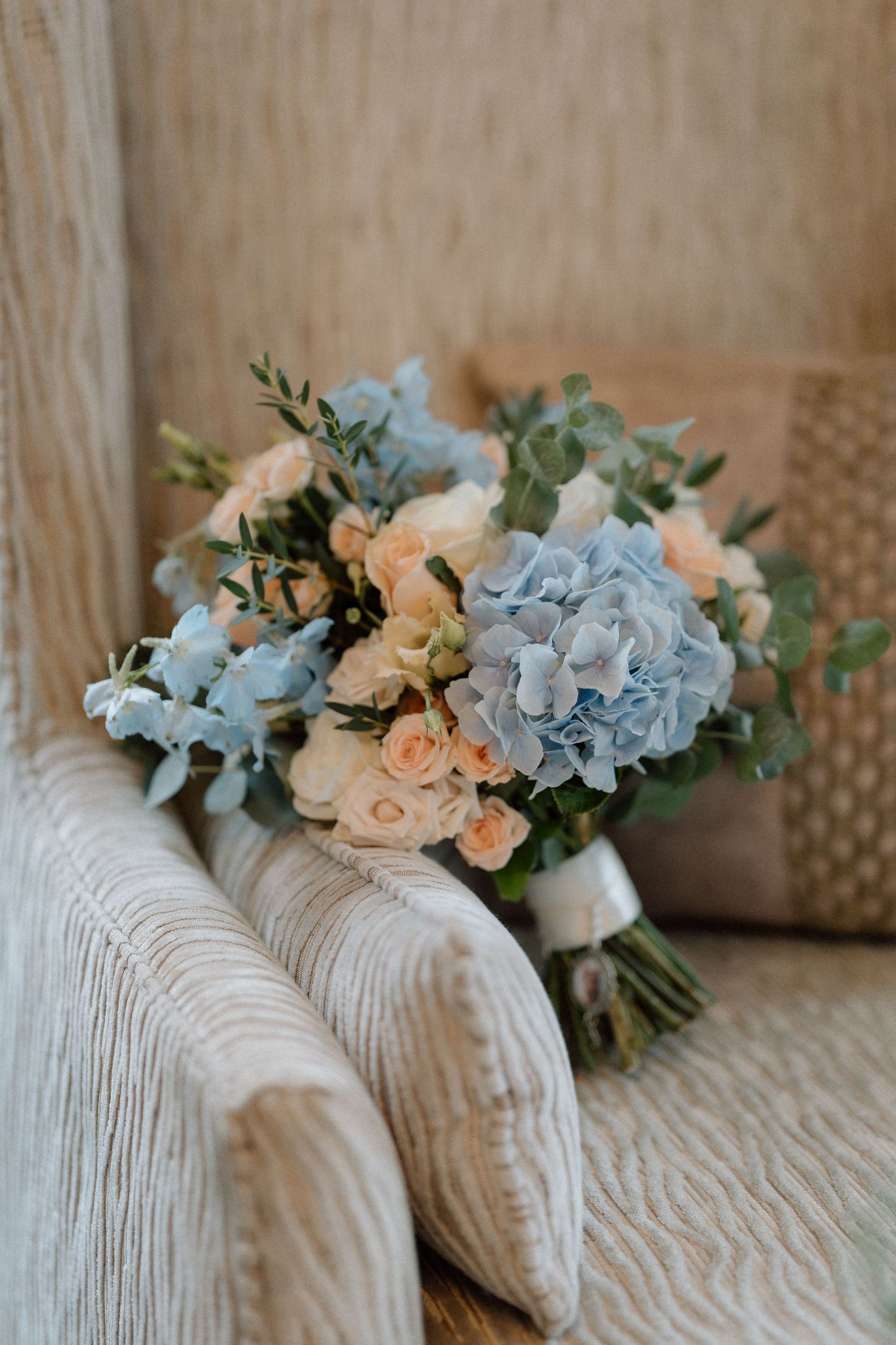 A romantic bouquet featuring light blue hydrangeas, peach roses, and eucalyptus leaves at Bourton Hall.