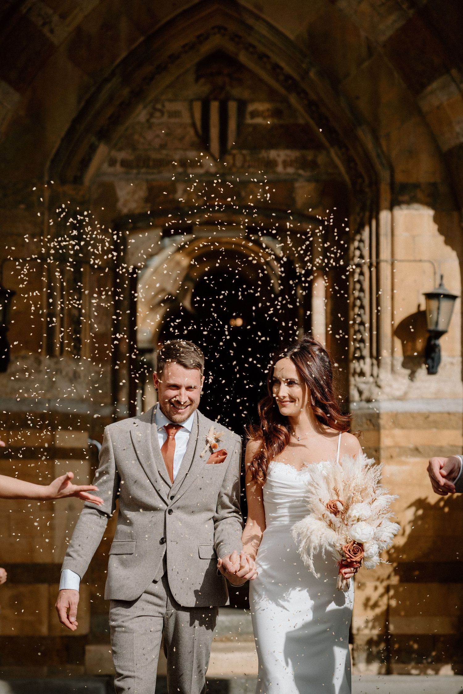 Couple celebrating with confetti outside historic stone church entrance.
