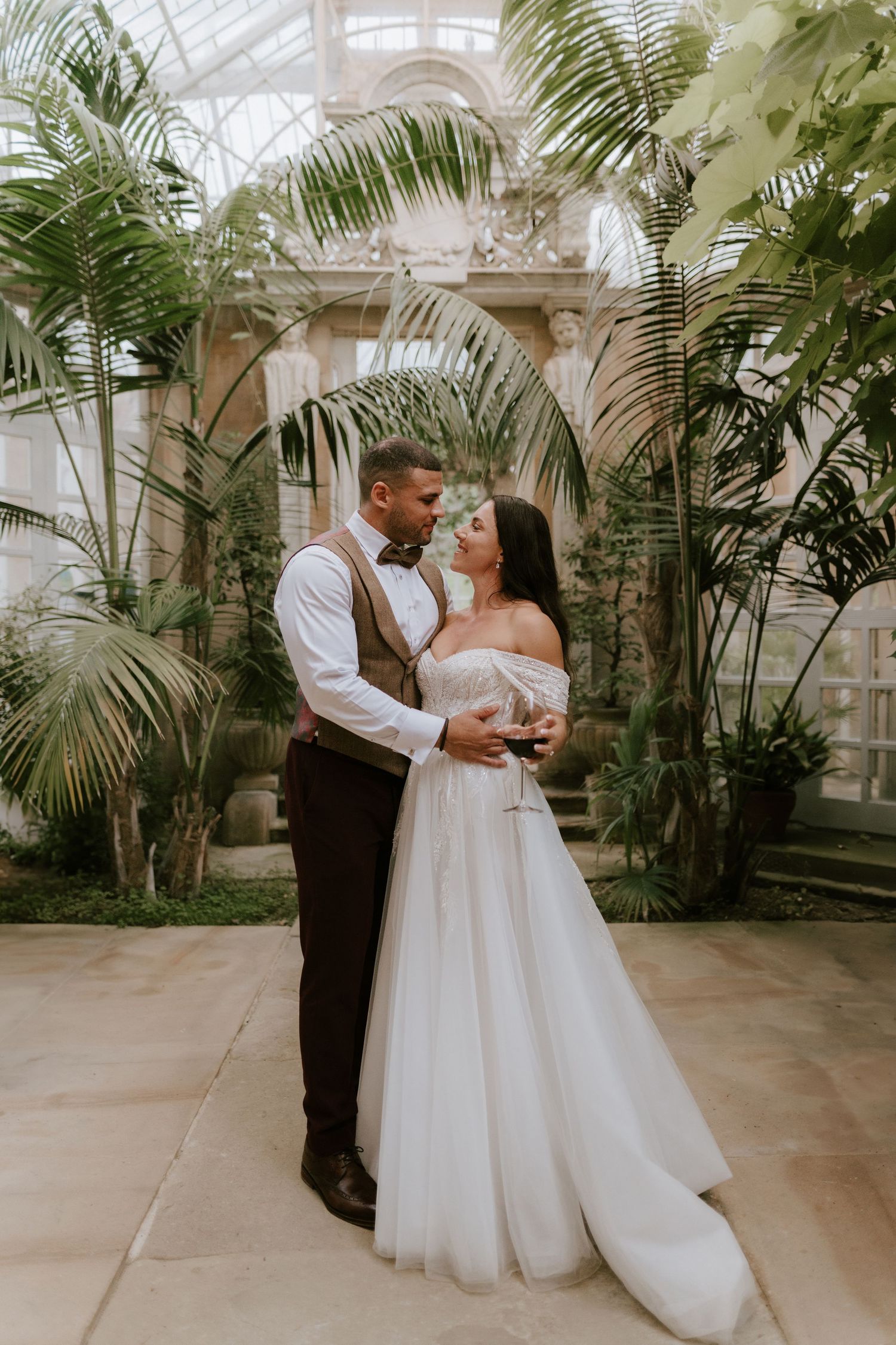 A romantic moment captured in a greenhouse filled with tropical palms and natural light at Harlaxton Manor.