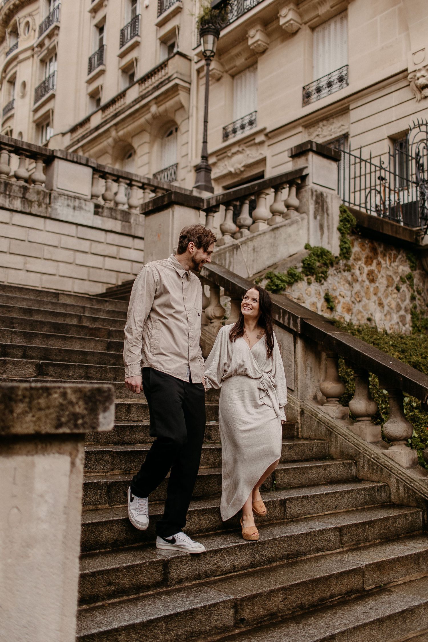 A couple descending elegant stone steps in matching neutral outfits near a Parisian building.