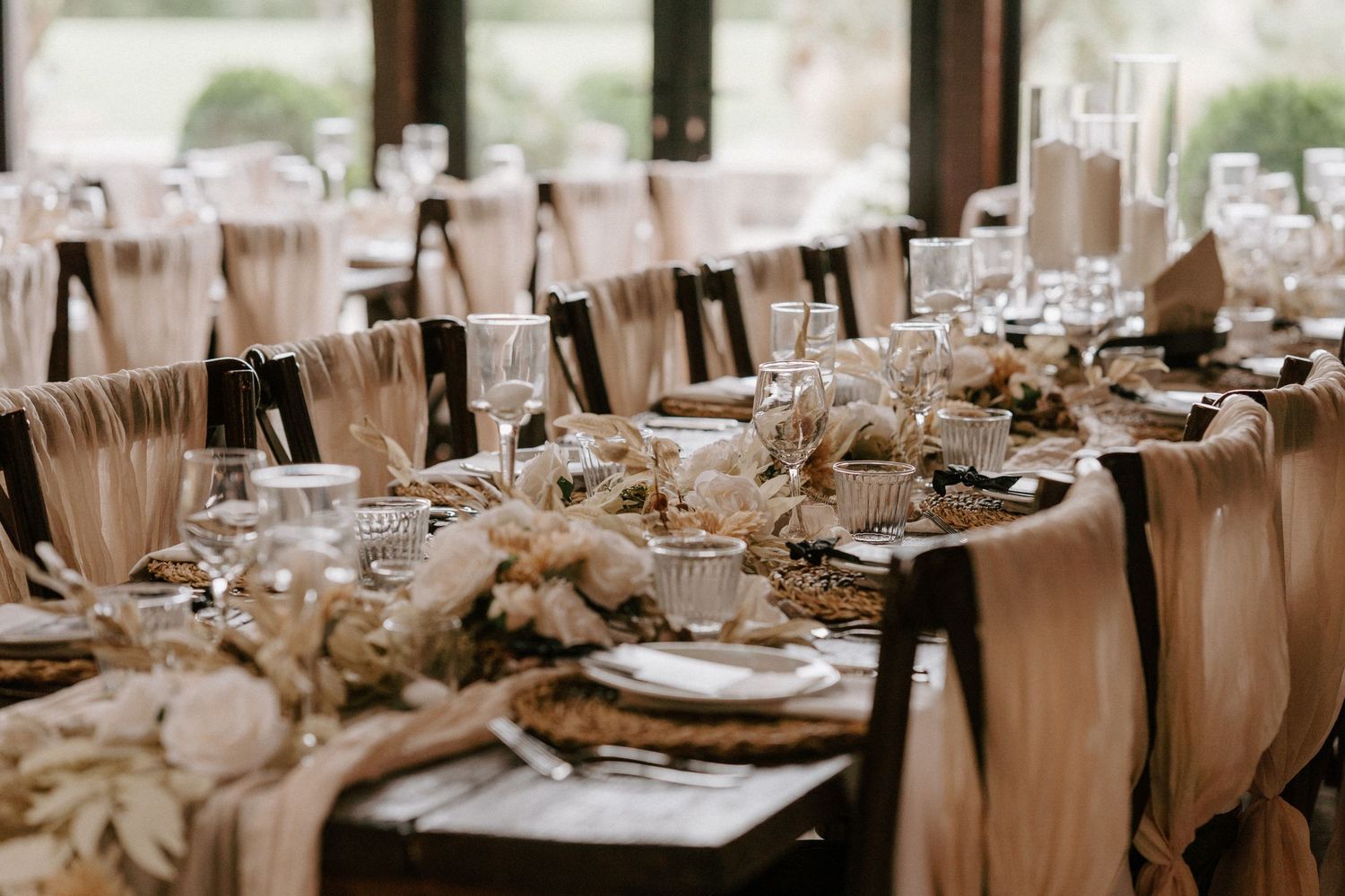 Elegant wedding reception table setup with tan linens, floral centerpieces and formal place settings in natural light, at Willow Marsh Farm