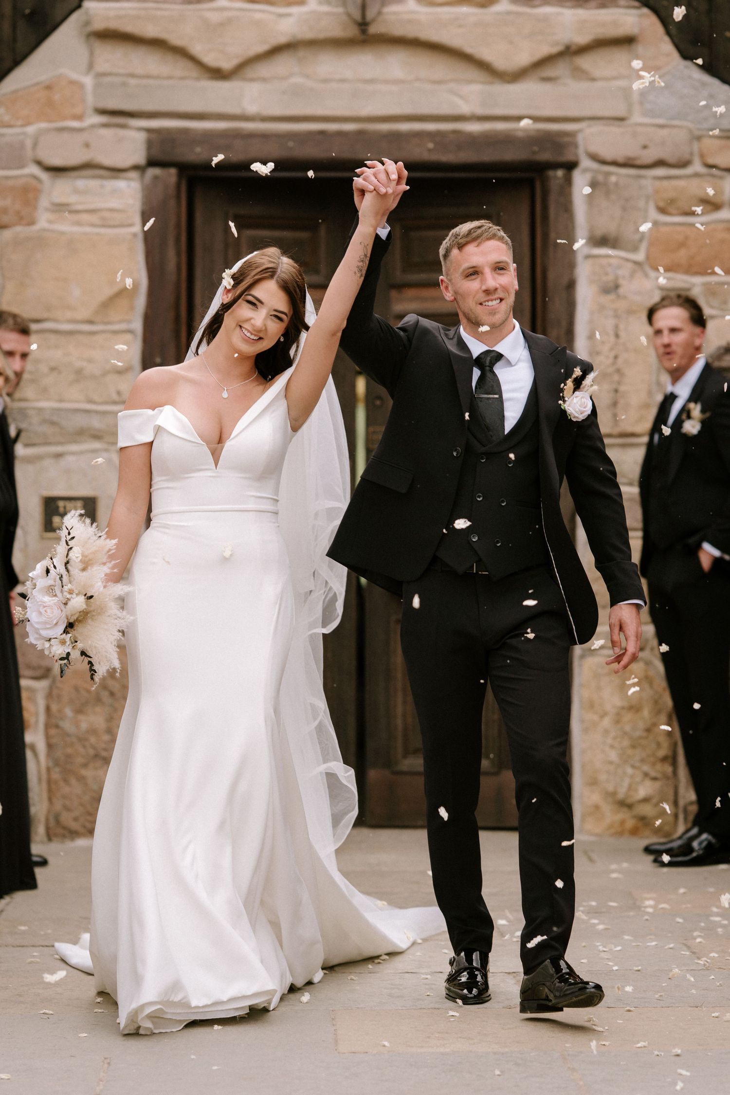 Wedding couple exits church ceremony as guests shower them with white confetti petals.Wedding photography at Willow Marsh Farm.