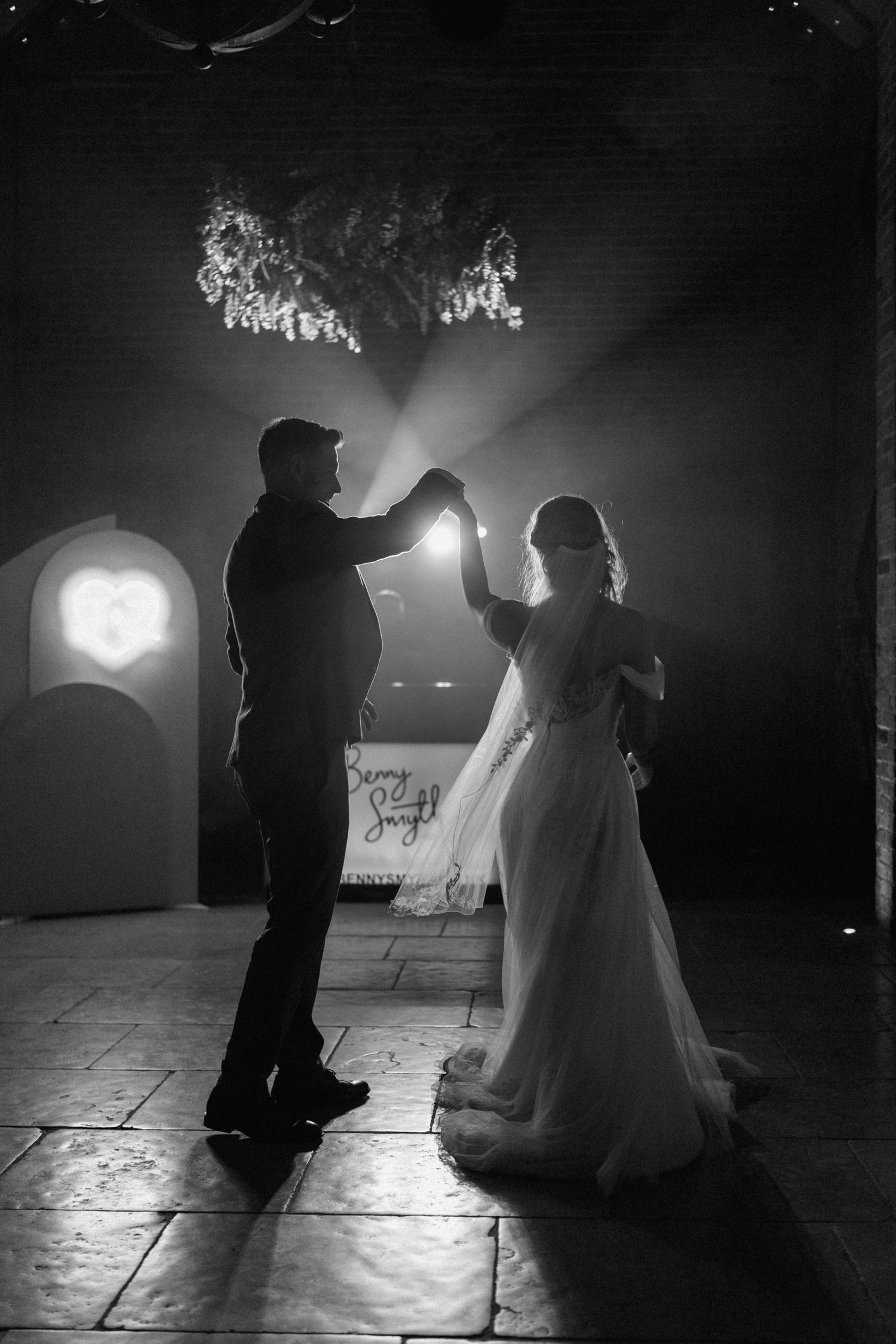 Silhouettes of a dancing couple in wedding attire against dramatic lighting on a stone floor at Shustoke Barn.
