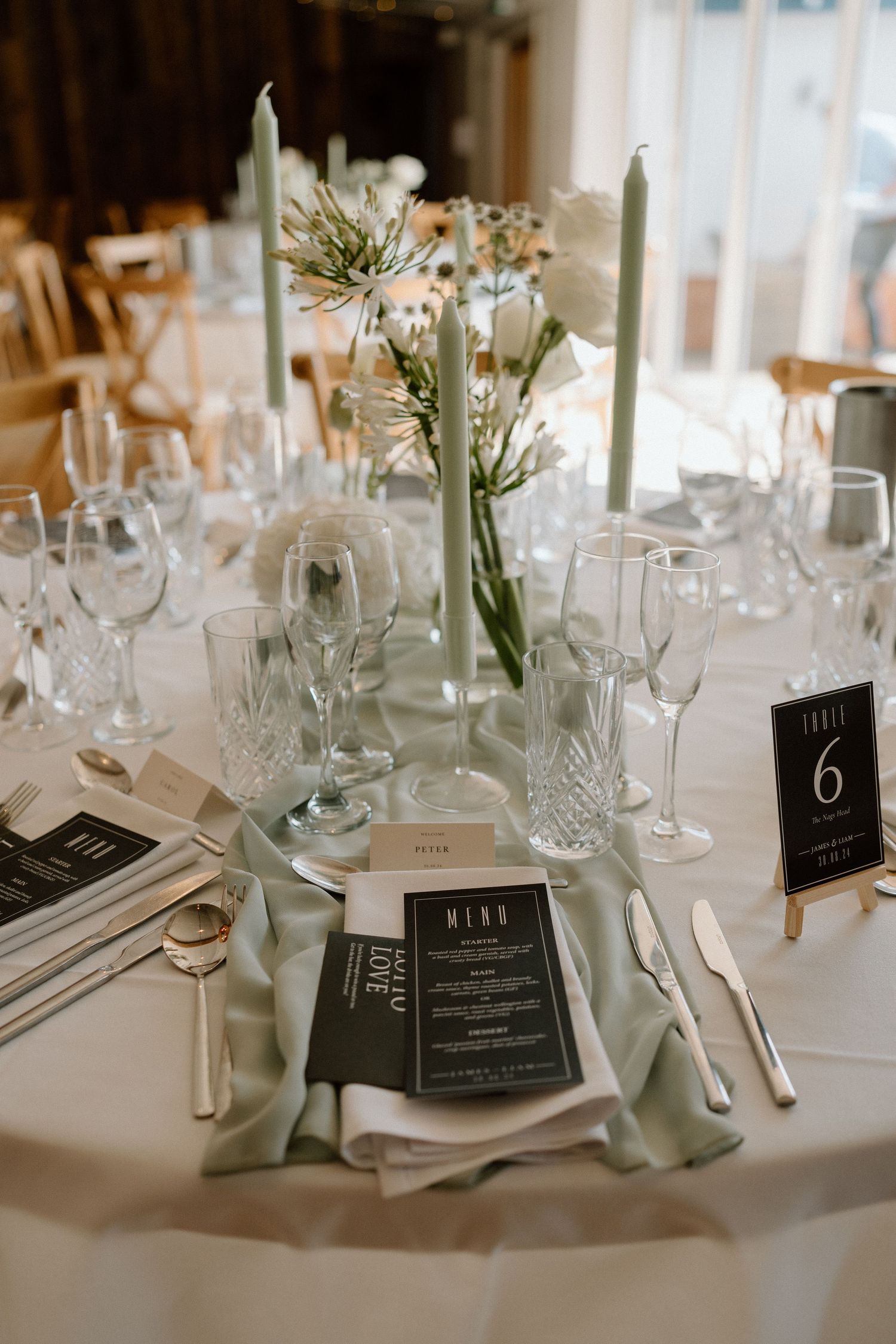 Elegant wedding table setting with white flowers, tall candles and modern menu cards.