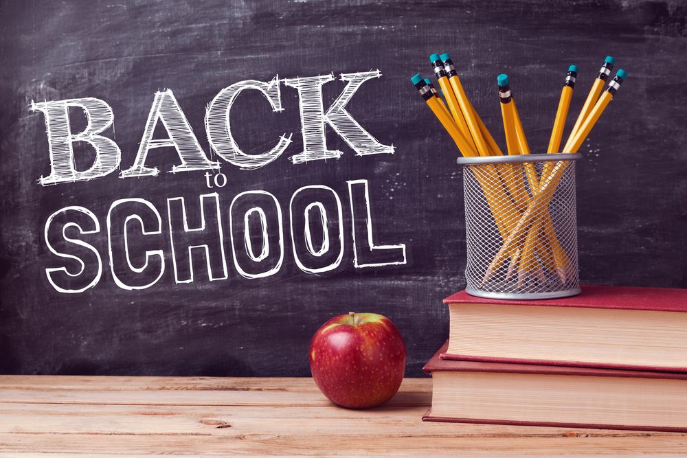 Colorful pencils and a red apple on wooden desk against chalkboard with 'Back to School' text.