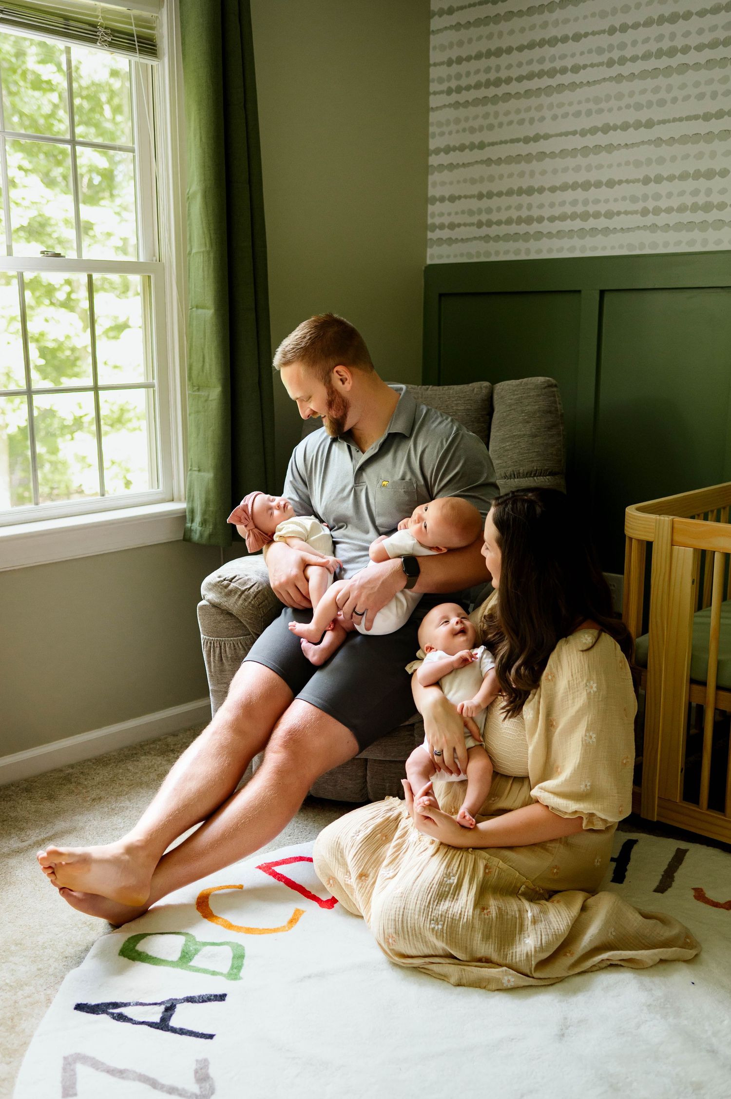 Family relaxes together on comfortable floor pillows in a cozy green room with triplet babies with wake forest newborn photographer