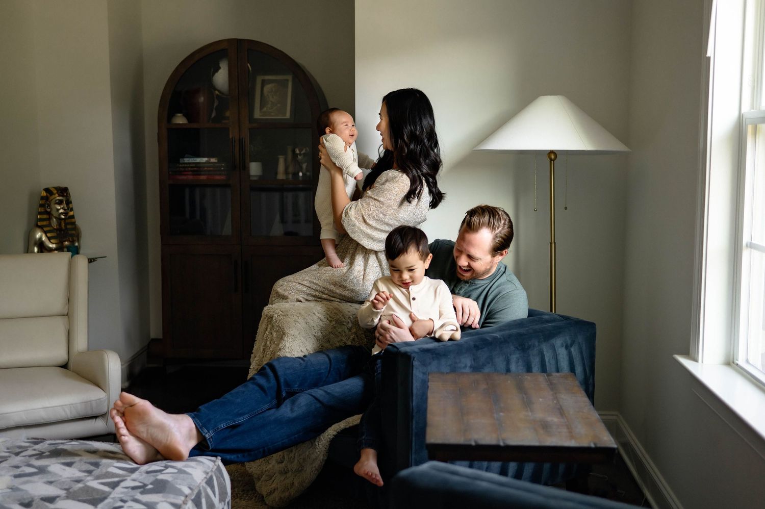 A family cuddles and smiles together in a cozy living room with natural light in their home during family photography session in raleigh