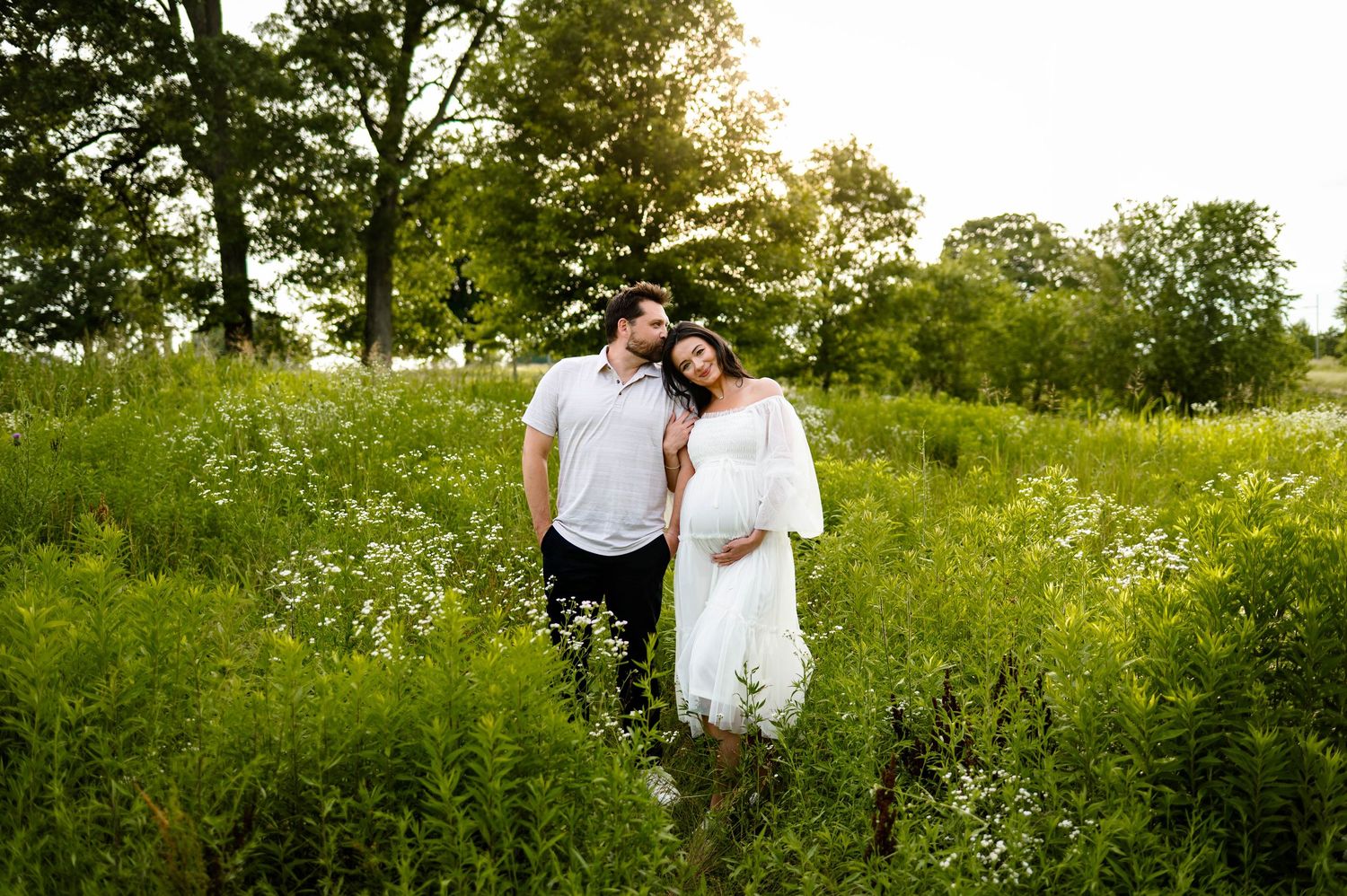 A romantic couple moment captured in a sunlit green field on a bright summer day for photo with raleigh maternity photographer