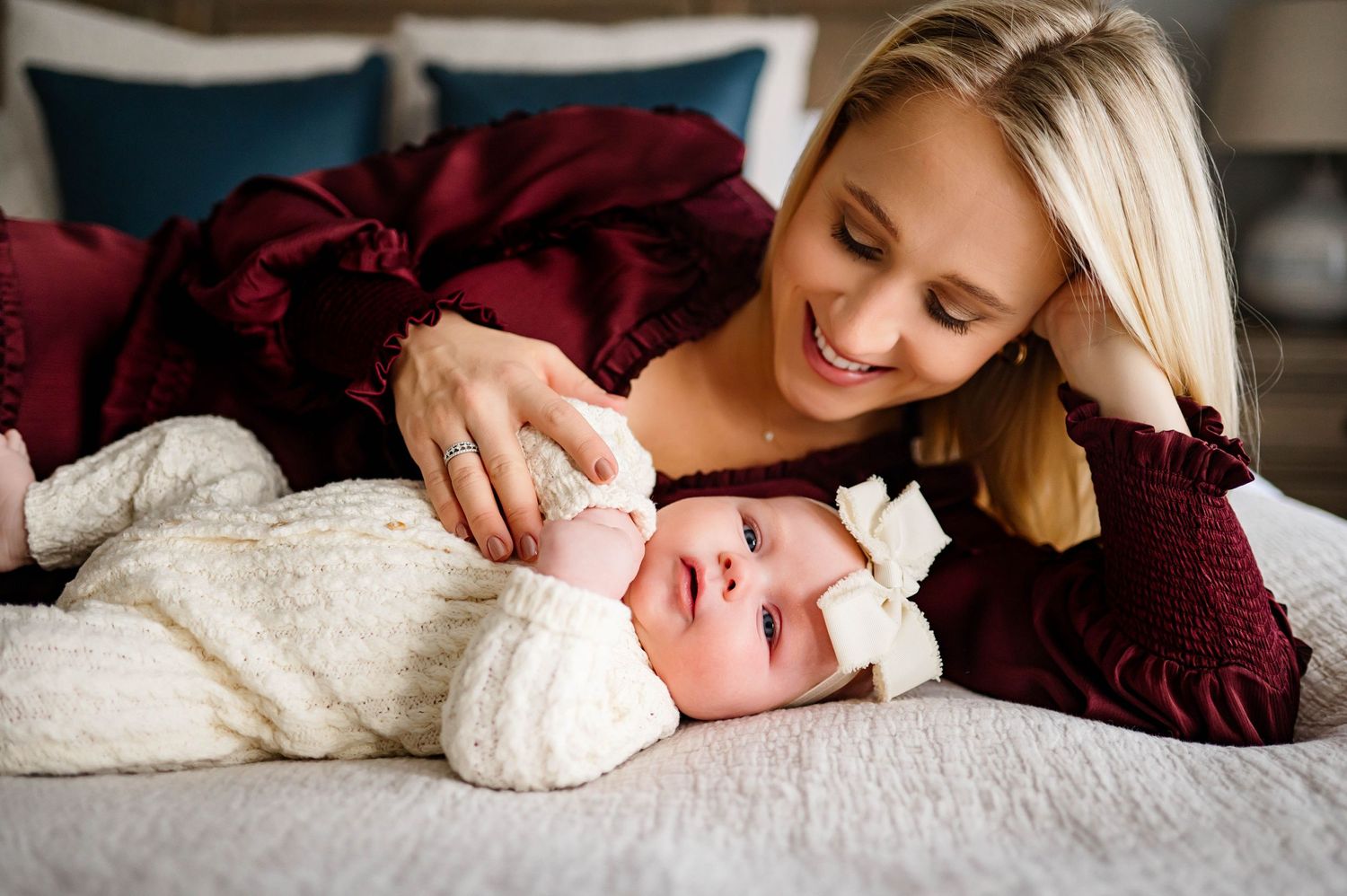Tender moment between mother and daughter lying on bed while mother plays gently with hands with best newborn photographer wake forest