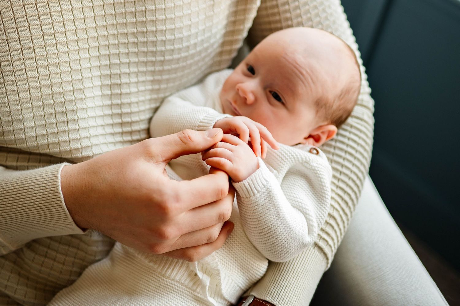 A small baby in a white onesie rests comfortably in father's arms during intimate newborn session with best raleigh newborn photographer