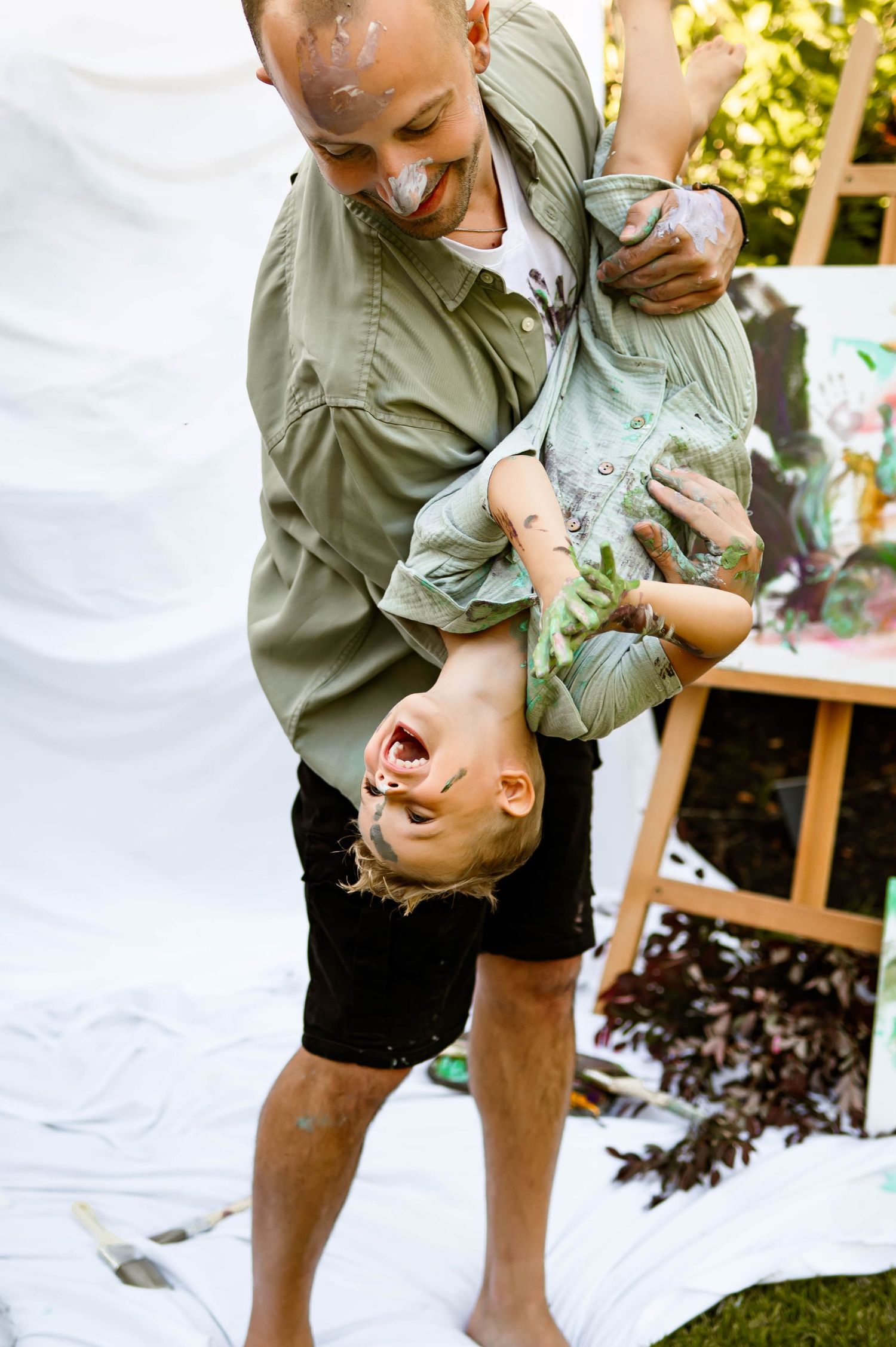 A father flips laughing son upside down playfully while covered in paint during family photography session with raleigh photographer