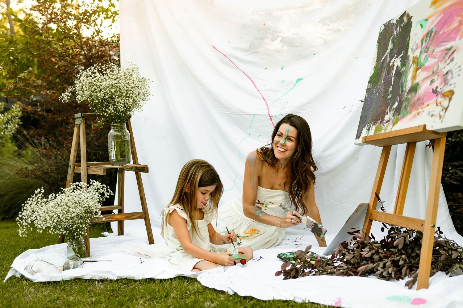 Mother and daughter sit on a blanket with art easels and baby's breath flowers scattered around them with affordable raleigh photographer