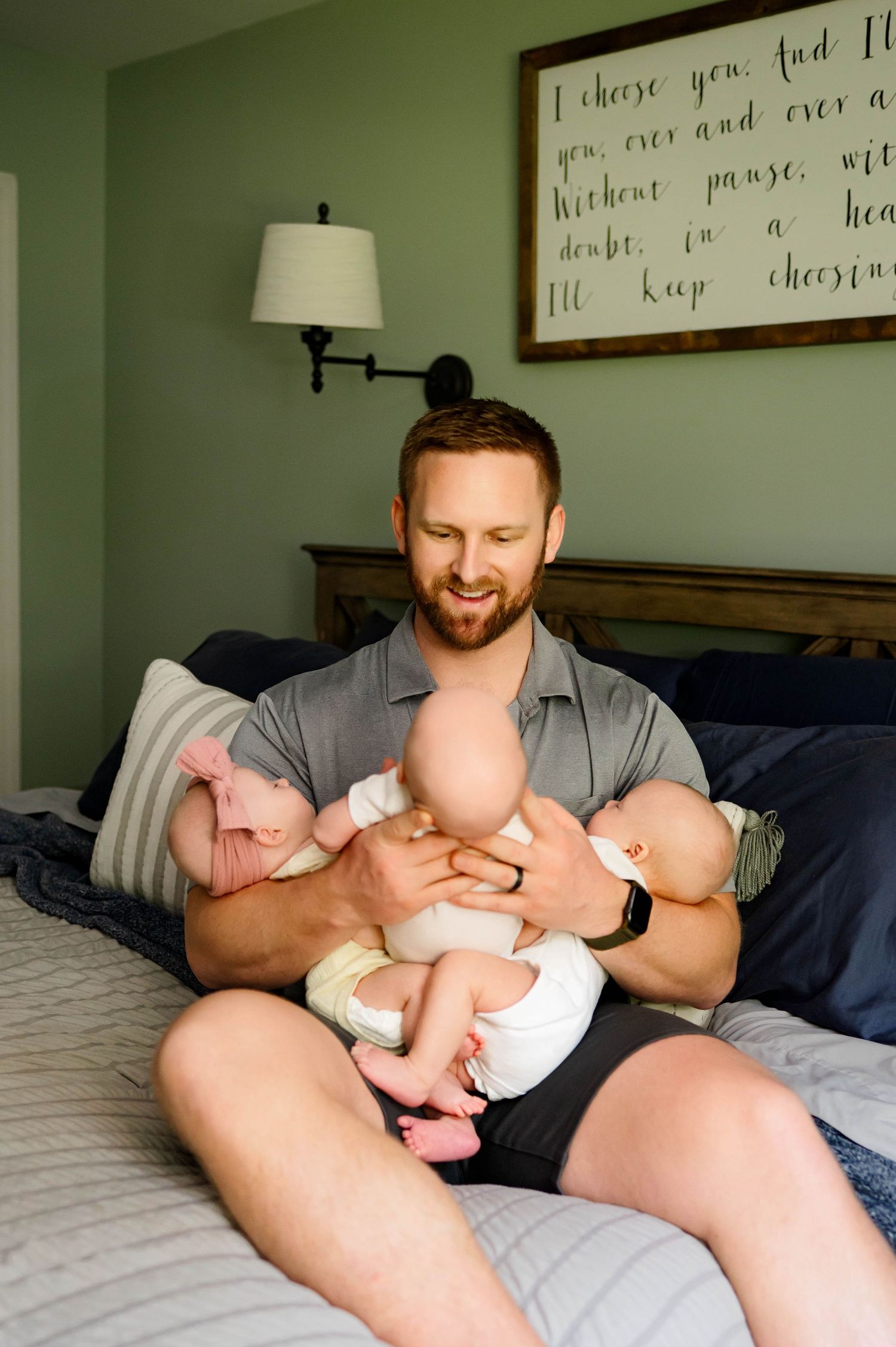 Father holds his triplet newborn babies and smiles tenderly at them in photograph by raleigh newborn photographer