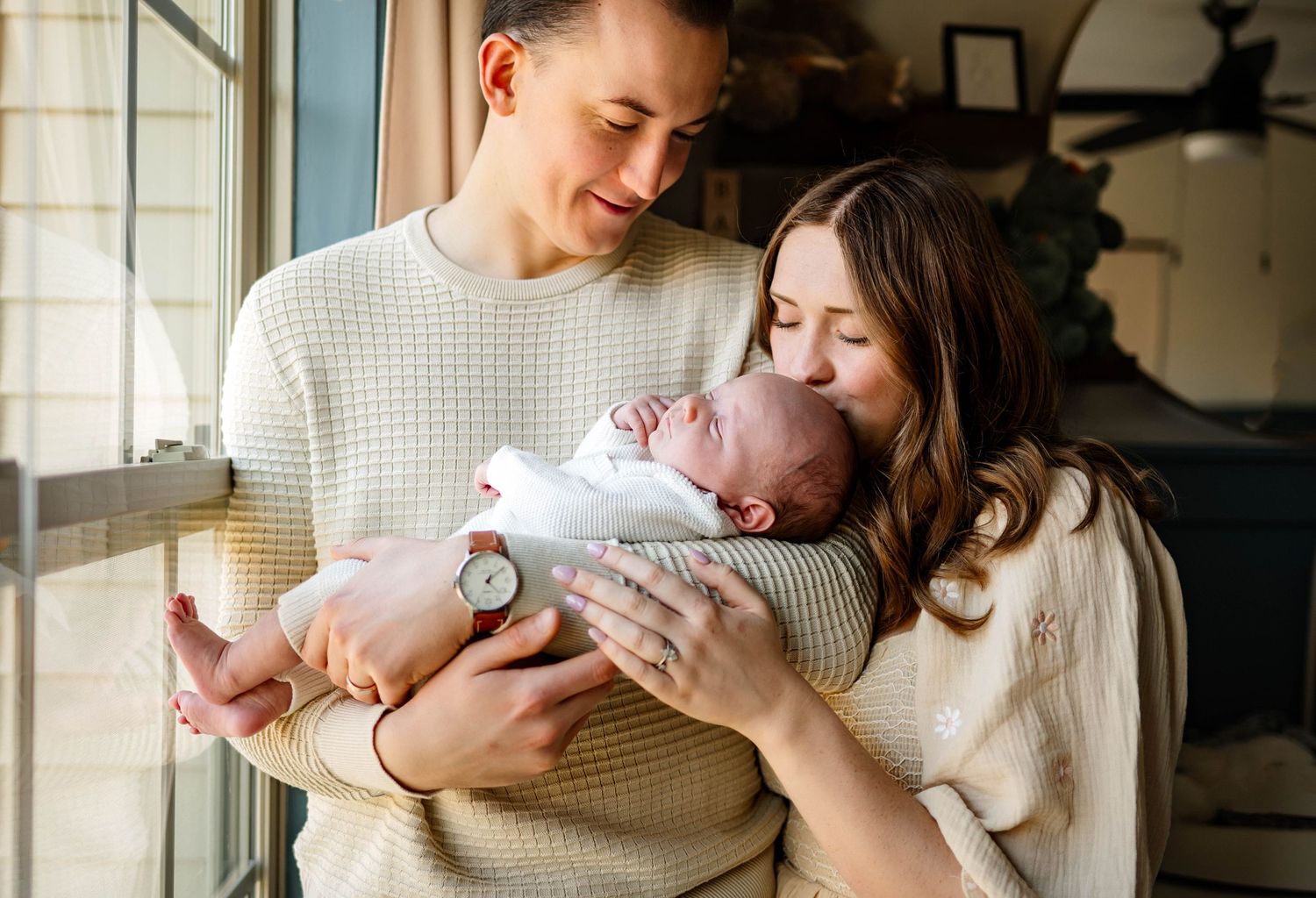 Parents holding their sleeping newborn baby near a window in natural light in the nursery for a photoshoot with Emma Branch Photography
