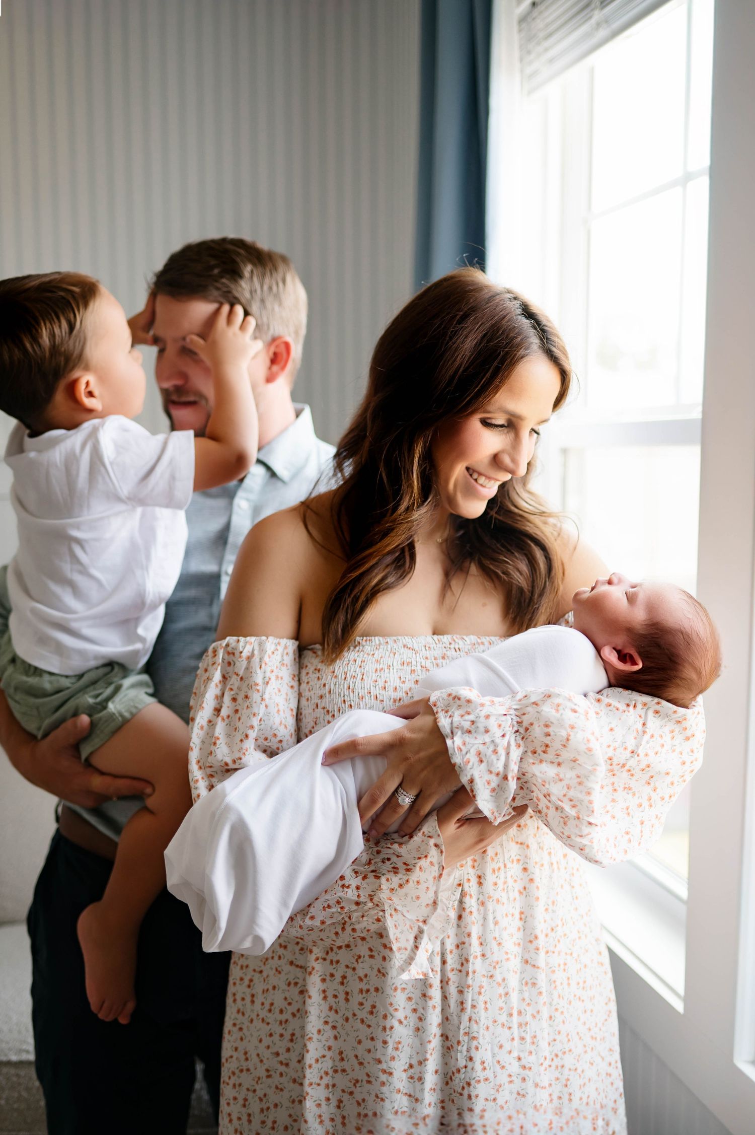 A joyful family moment captured by a window, with heartwarming interactions in natural light with the best Wake Forest Newborn Photographer