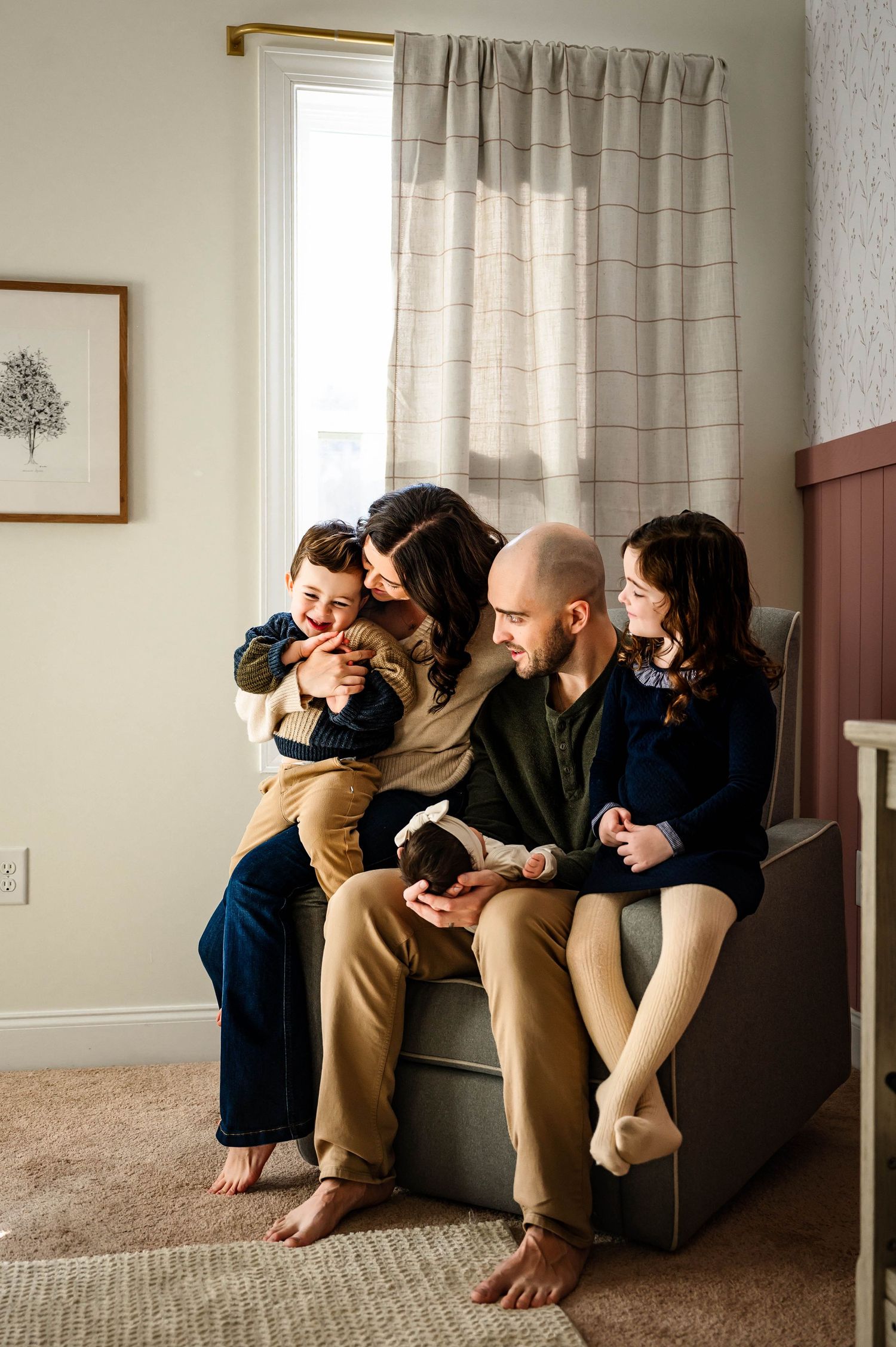 A cozy family moment at home on a chair, sharing cuddles and smiles in natural window lighting in nursery with Emma Branch Photography