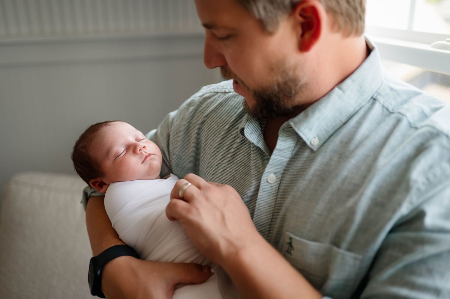A tender moment between a father and newborn baby swaddled in white in soft lighting in nursery during newborn photoshoot apex nc