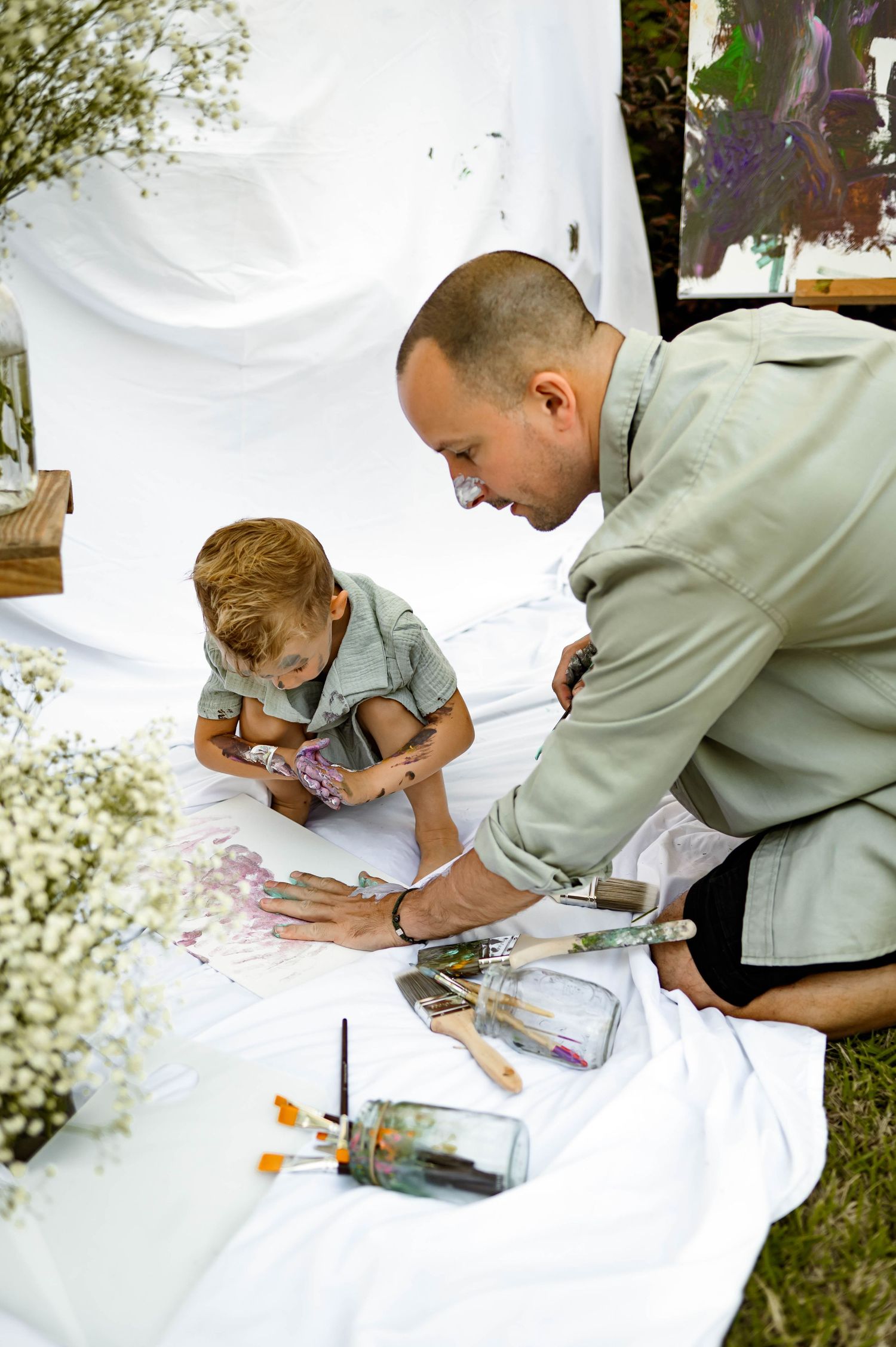 Father and son painting together on a white sheet outdoors during a creative activity with raleigh family photographer