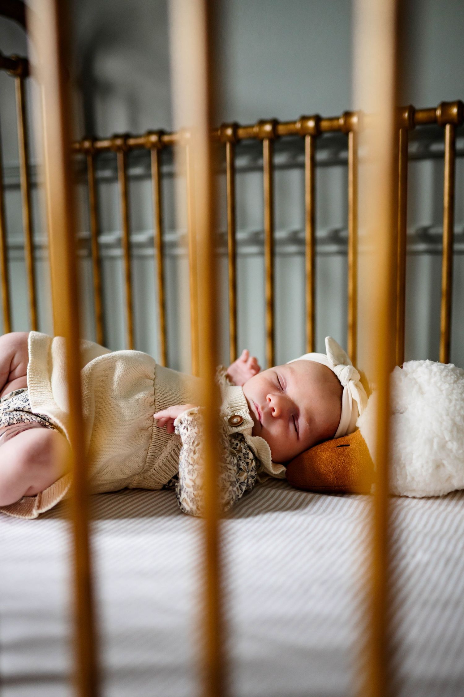 Sleeping newborn wearing cream knit outfit rests peacefully in wooden crib with wake forest nc newborn photographer