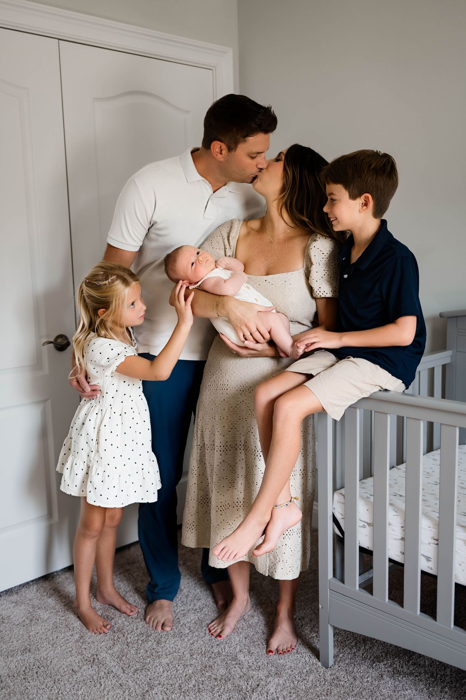 A loving family with three children stands together in a nursery room with gray carpet and white walls with Emma Branch Photography