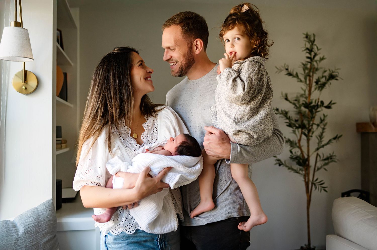 Parents sharing a joyful moment with their newborn baby and toddler by a bright window at home with the best newborn photographer durham