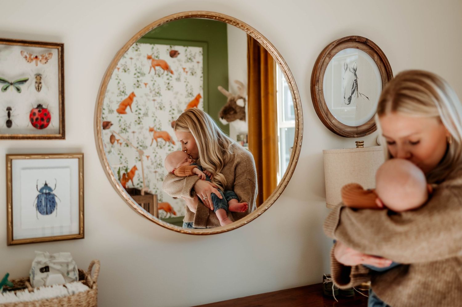 Circular mirror on wall reflects mother and newborn son in cozy nursery during a photography session with raleigh newborn photographer