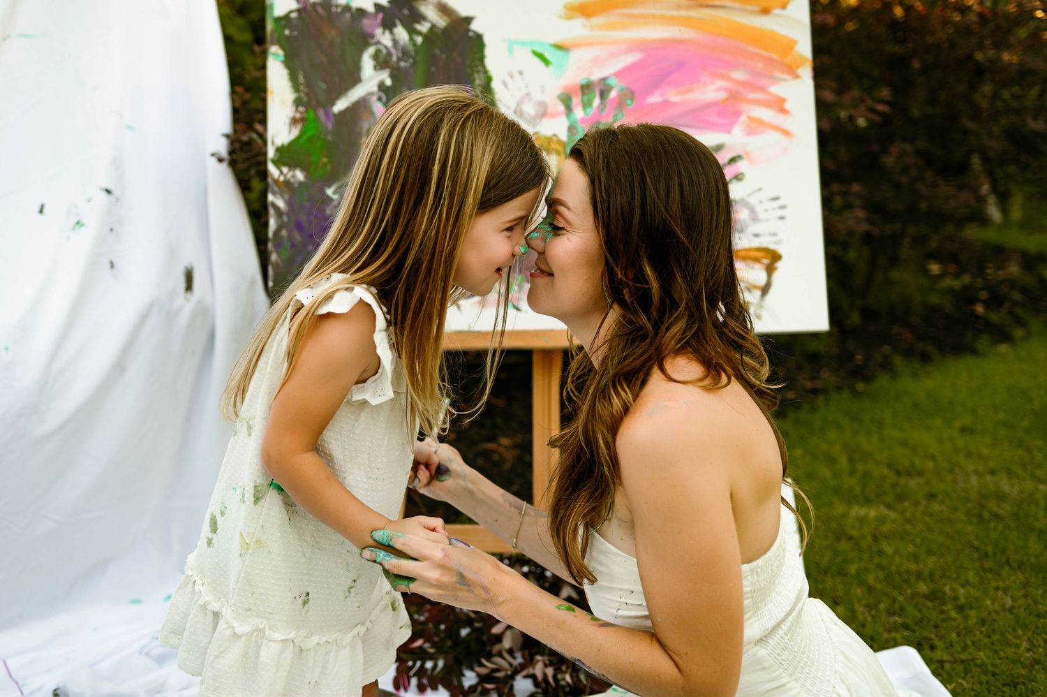 A tender moment between mother and daughter in front of a colorful painted backdrop during outdoor family photography session in raleigh nc