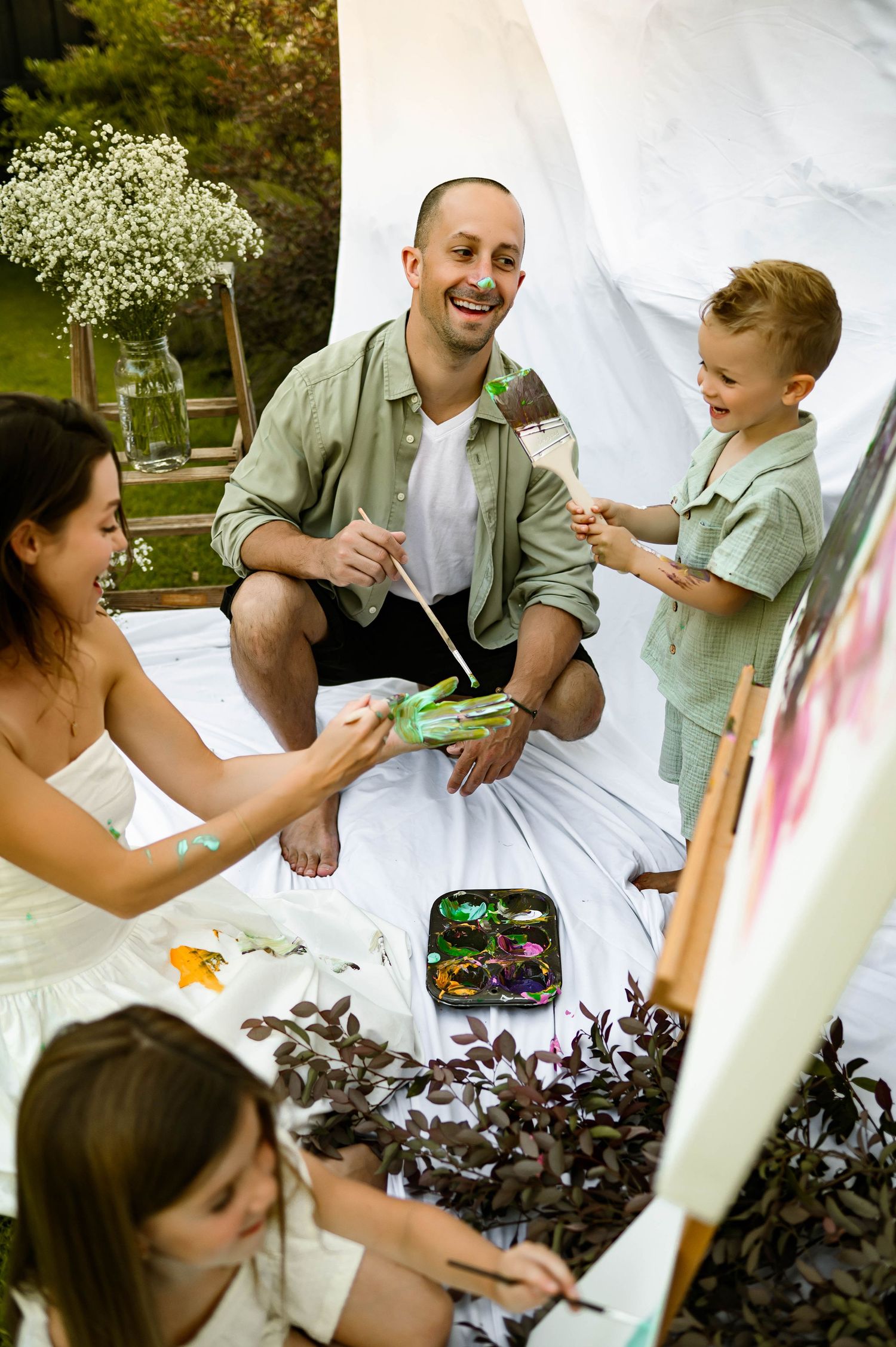 A family gathering on a blanket outdoors with flowers and decorative elements surrounding them during a fun family photography session